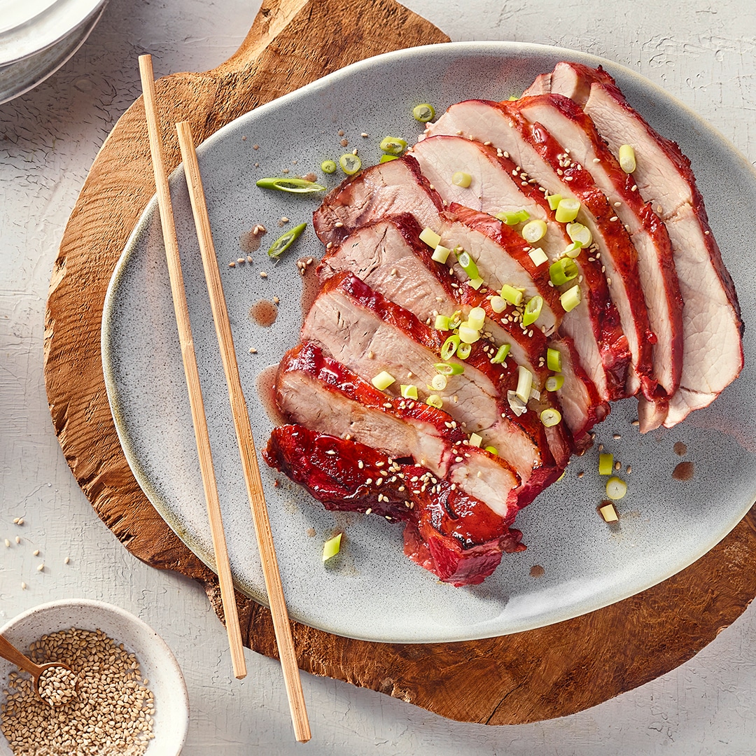 Teller mit geschnittenen und glasierten Fleischscheiben und Frühlingszwiebelringen