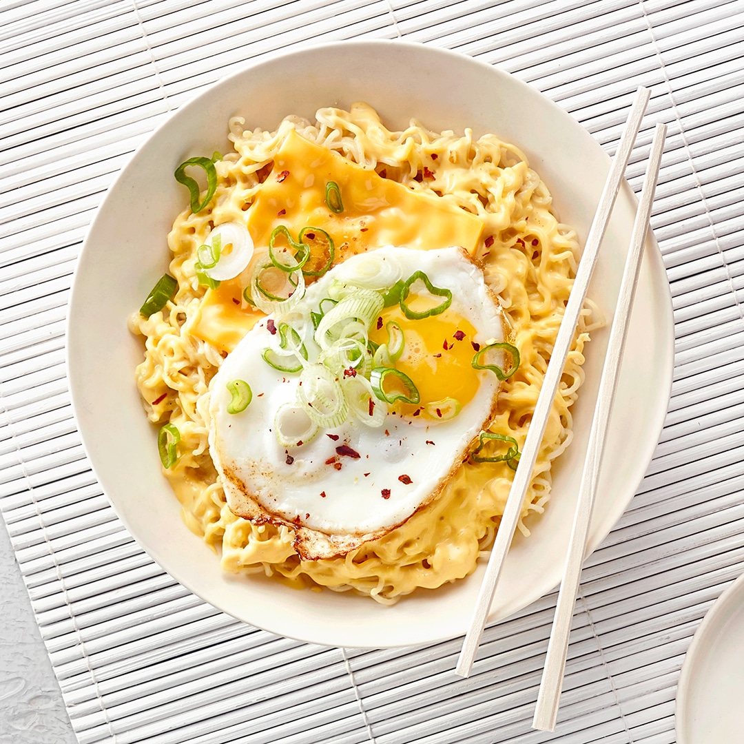 Instant-Nudeln mit Käse, Spiegelei und Frühlingszwiebeln, dazu Essstäbchen.