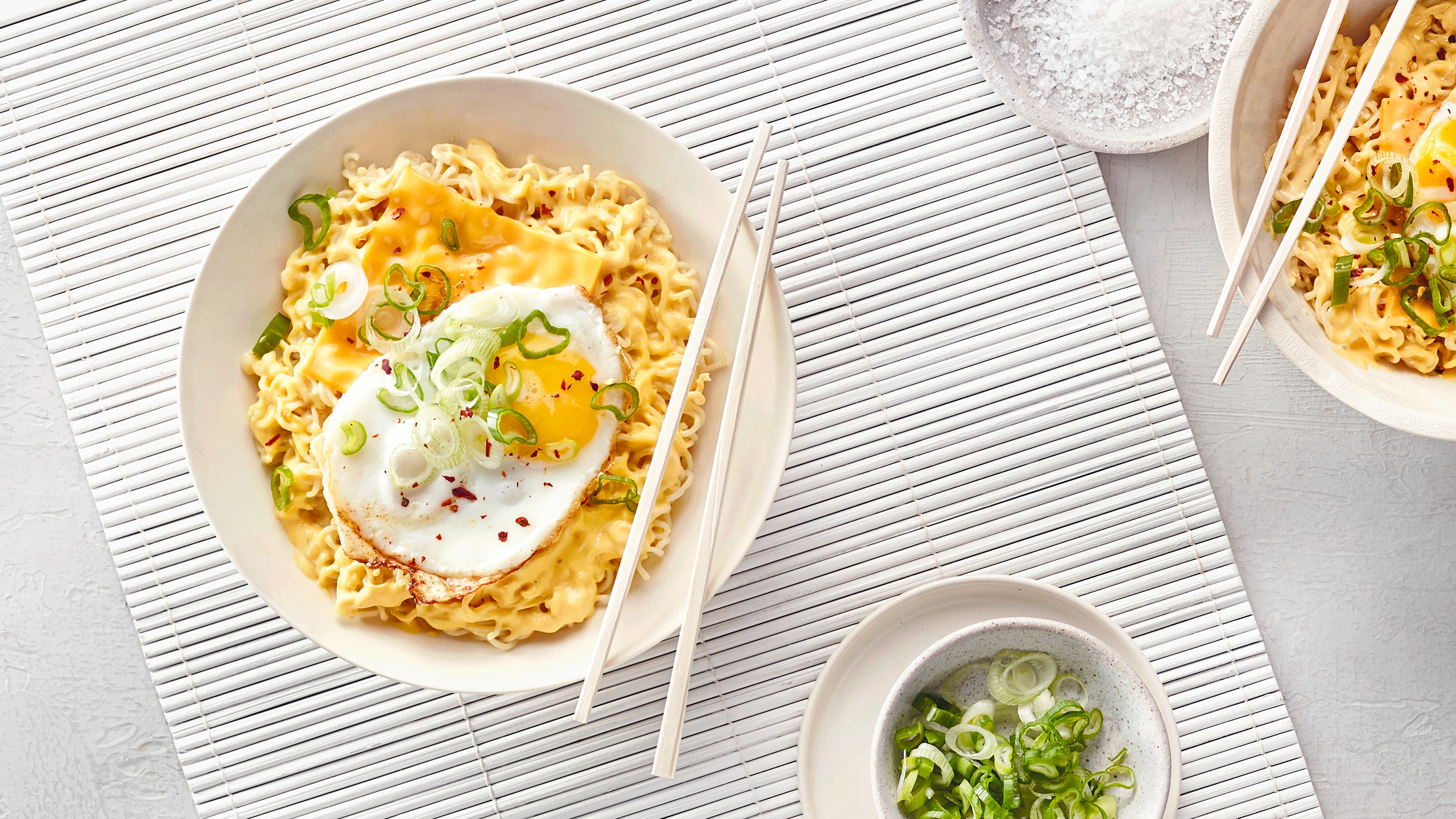 Instant-Nudeln mit Käse, Spiegelei und Frühlingszwiebeln, dazu Essstäbchen.