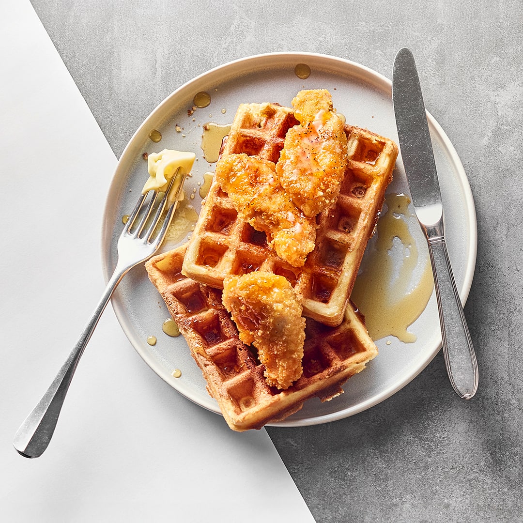 Rechteckige fluffige Waffeln, getoppt mit knusprig frittierten Hähnchennuggets, Butter und flüssigem Honig, auf einem Teller