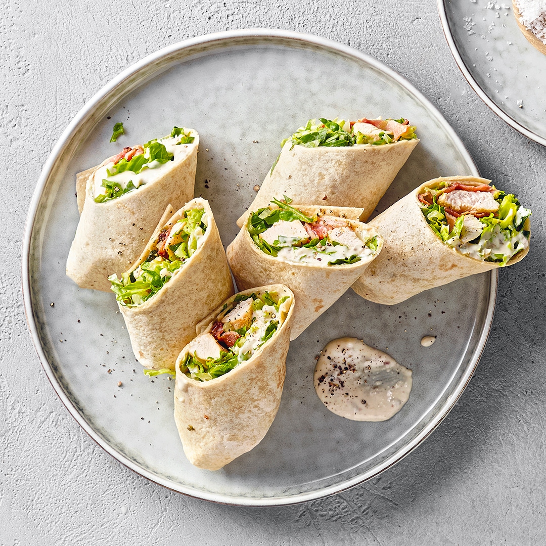Teller mit gerollten Wraphälften, gefüllt mit Salat und Hähnchenstücken
