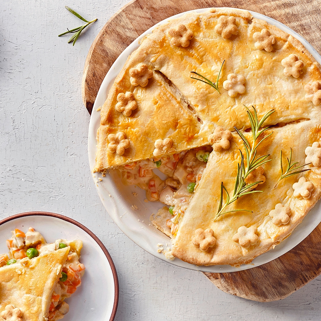 Ein Teller mit Pastete mit goldbrauner Kruste, verziert mit Teigblumen & Rosmarinzweigen, gefüllt mit Gemüse in cremiger Sauce