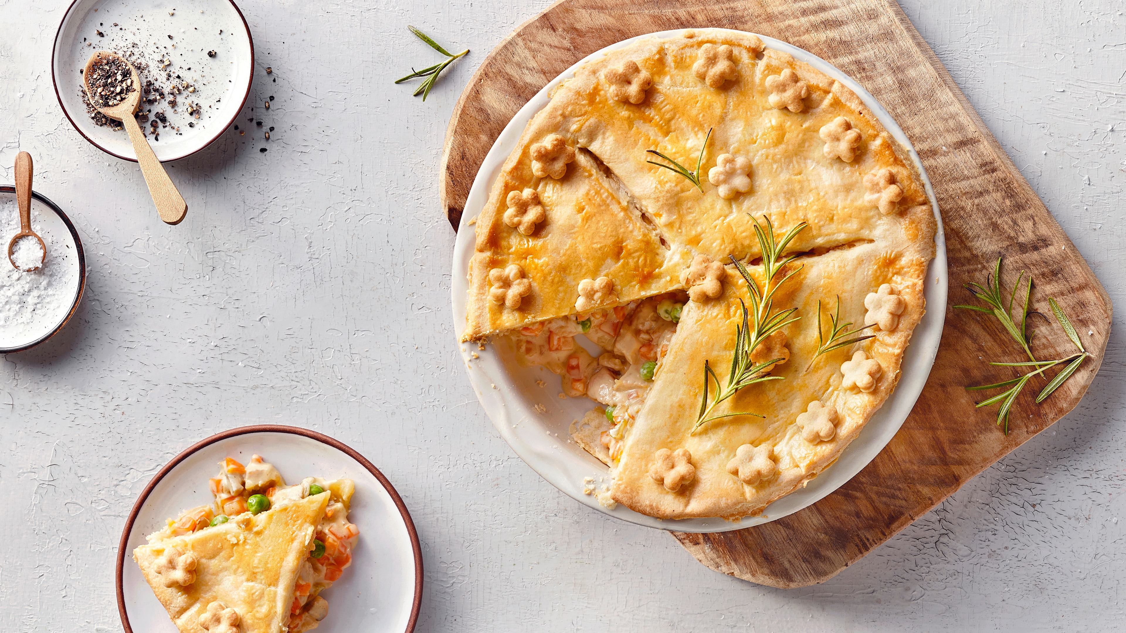 Ein Teller mit Pastete mit goldbrauner Kruste, verziert mit Teigblumen & Rosmarinzweigen, gefüllt mit Gemüse in cremiger Sauce