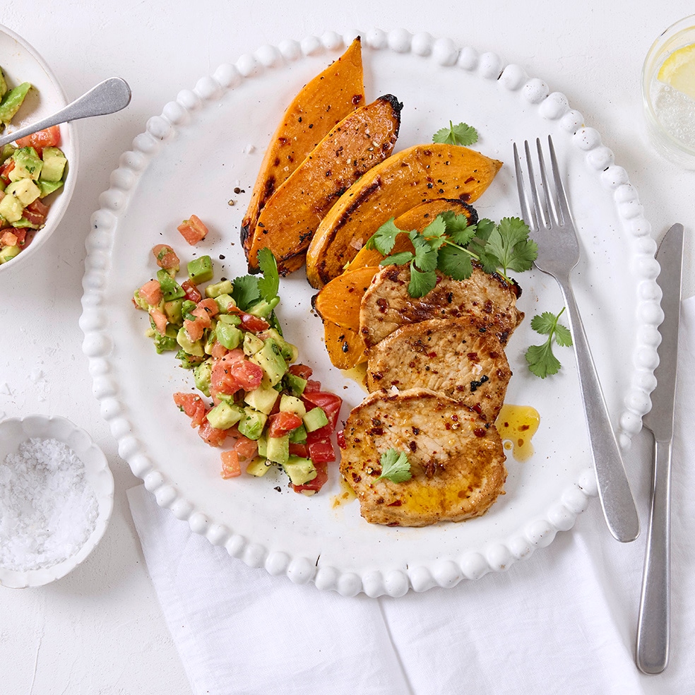 Gewürzte Schnitzel, Süßkartoffelscheiben und ein Avocado-Tomaten-Salat auf einem Teller