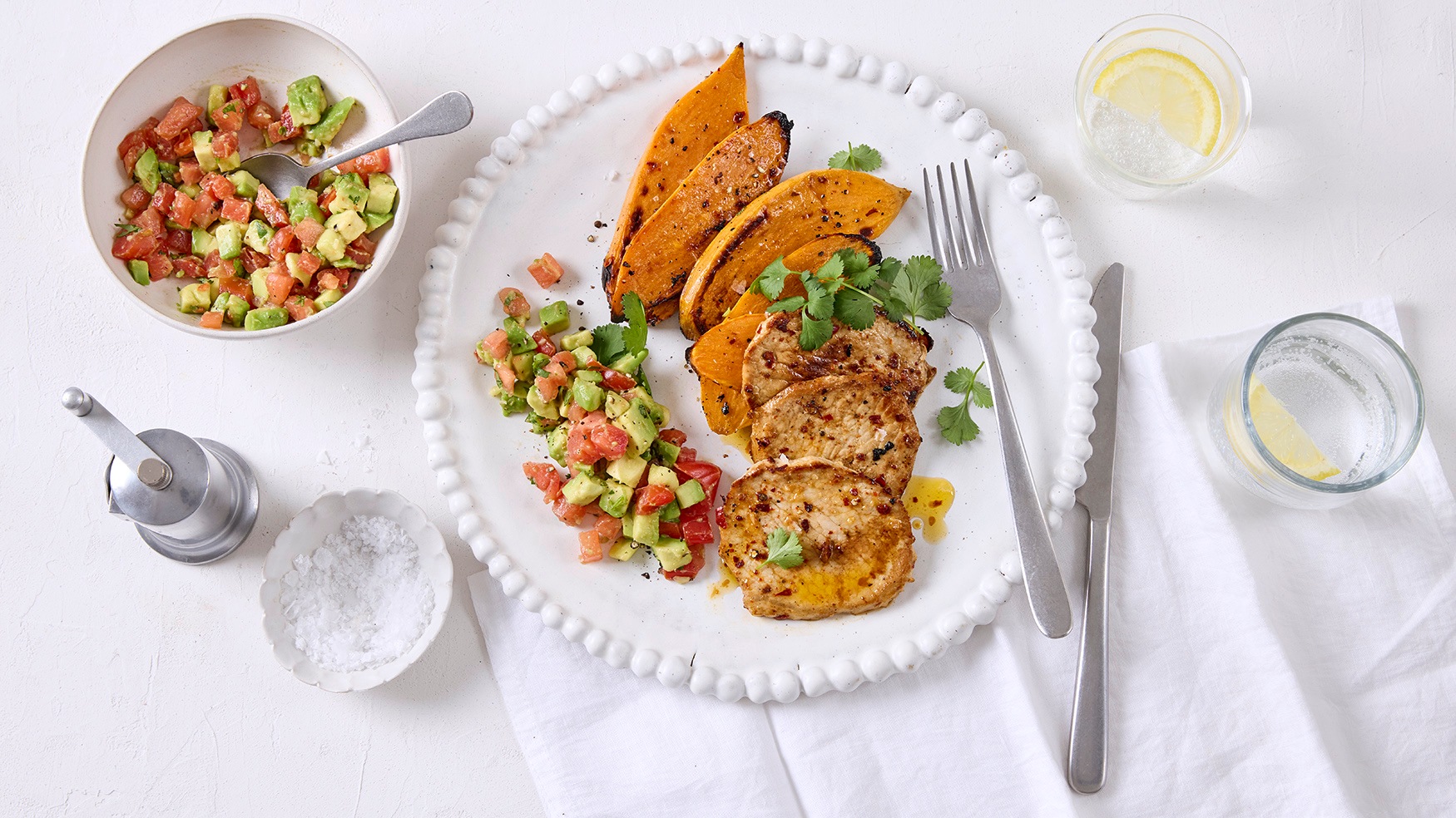 Rezept für Chili-Schnitzel mit Süßkartoffeln Gewürzte Schnitzel, Süßkartoffelscheiben und ein Avocado-Tomaten-Salat auf einem Teller