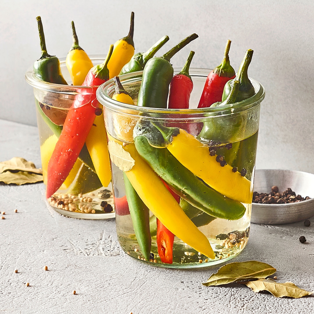 Zwei Einmachgläser gefüllt mit zahlreichen gelben, grünen und roten Chilis.