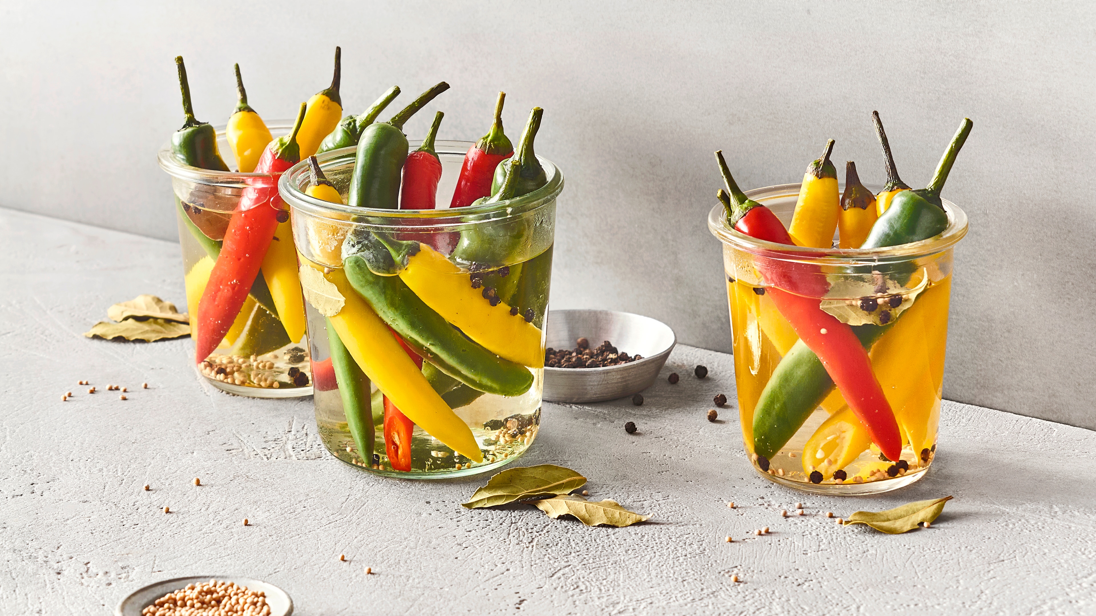 Drei Einmachgläser gefüllt mit zahlreichen gelben, grünen und roten Chilis.