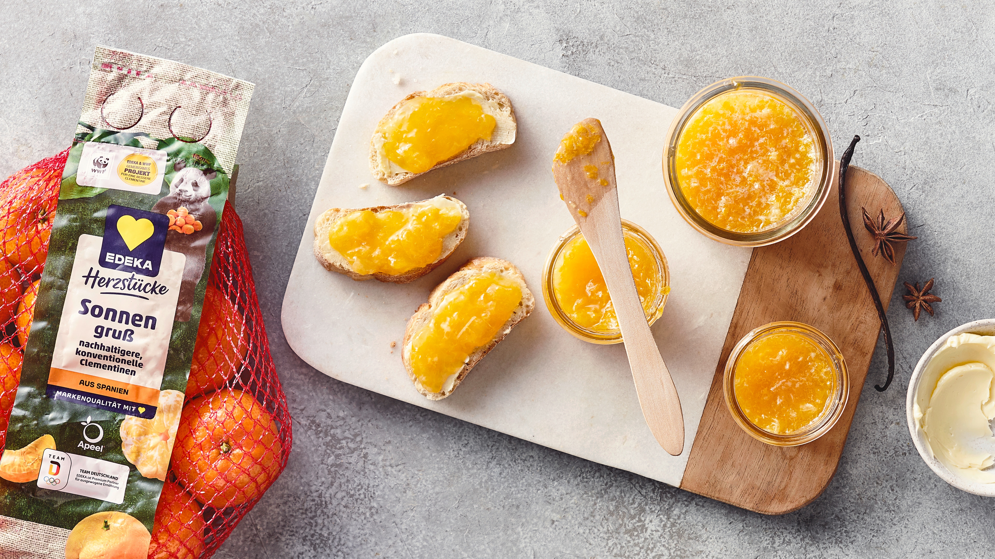 Ein Brett mit drei Brotscheiben, bestrichen mit gelbem Aufstrich, daneben Gläser mit Aufstrich und ein Holzmesser