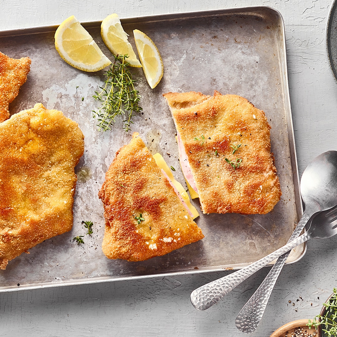 Panierte Schnitzel mit einer Schinken-Käse-Füllung auf Backblech.