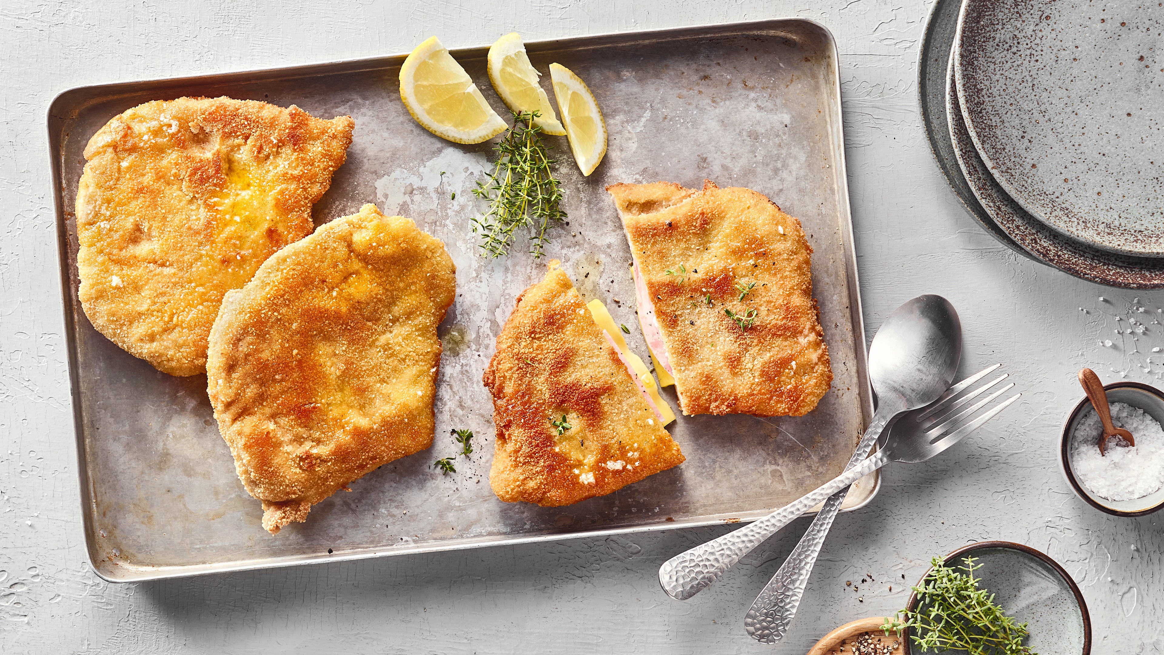 Drei panierte Schnitzel mit einer Schinken-Käse-Füllung auf Backblech.