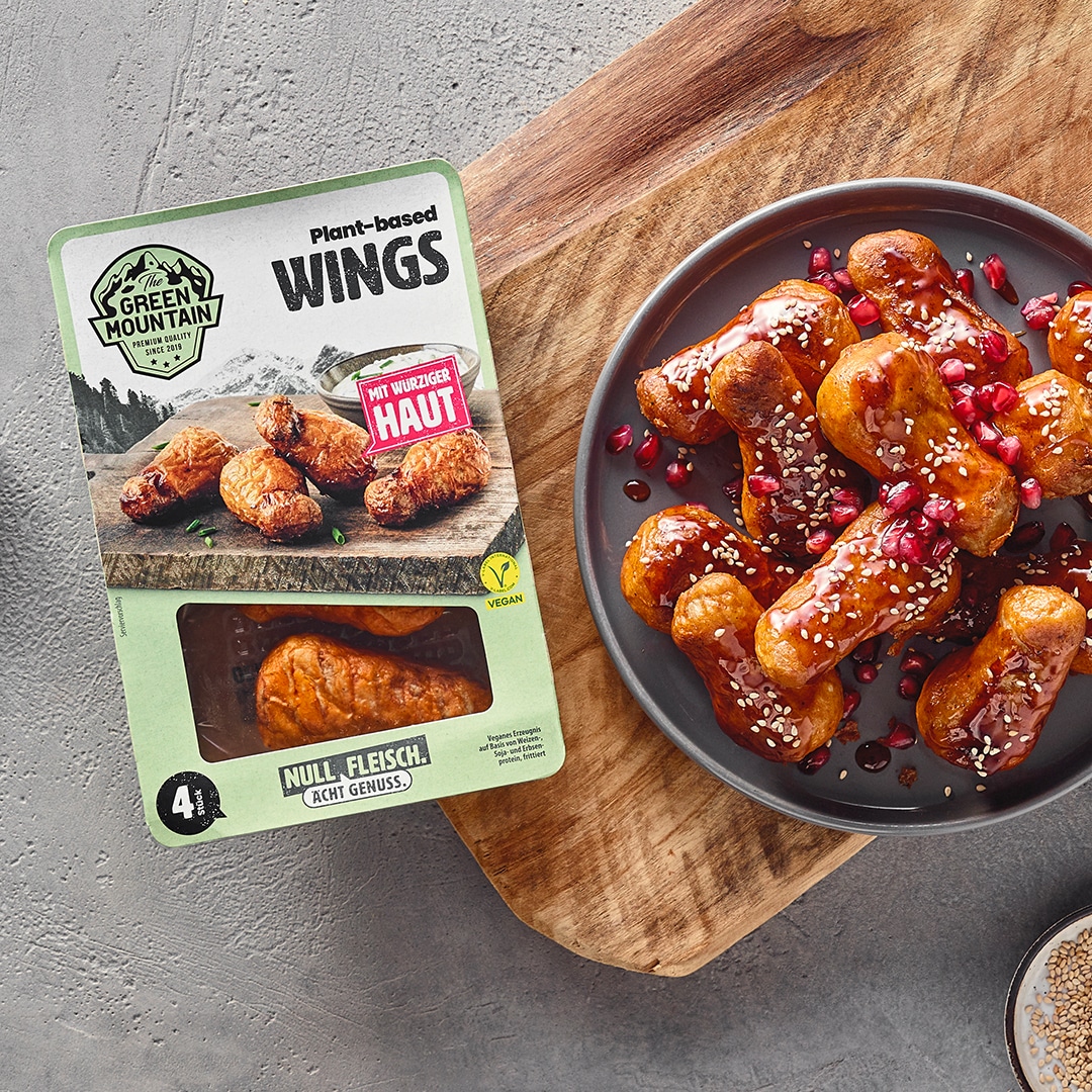 Ein Teller mit Wings in Panade, überzogen mit brauner Sauce, bestreut mit Sesam und Granatapfelkernen