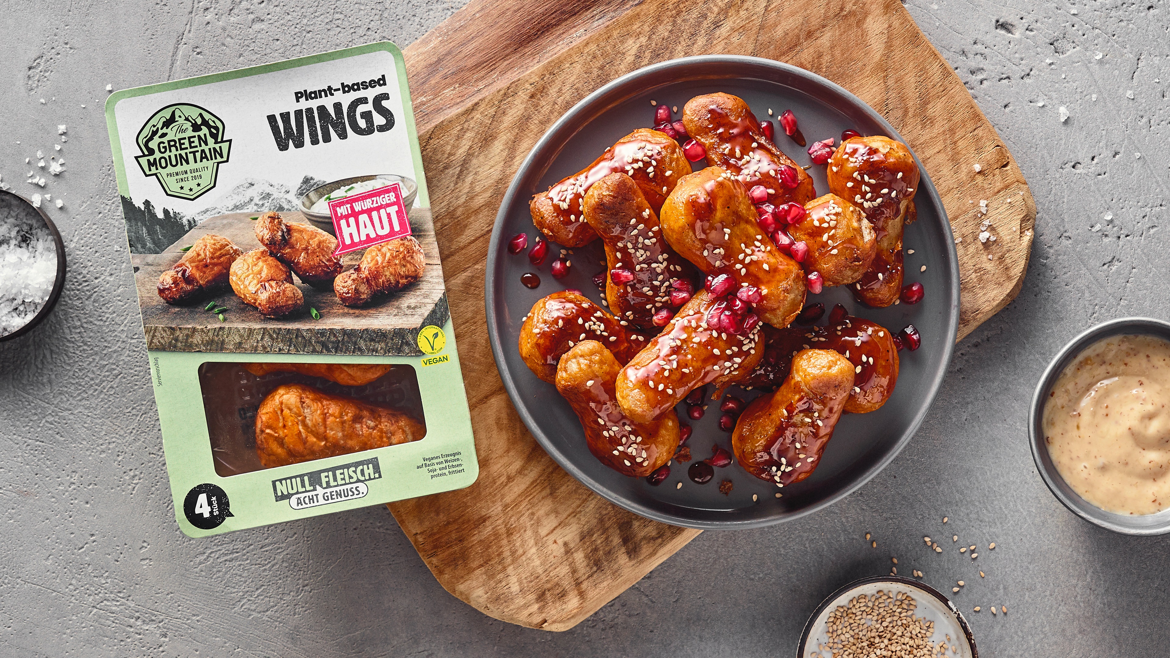 Ein Teller mit Wings in Panade, überzogen mit brauner Sauce, bestreut mit Sesam und Granatapfelkernen