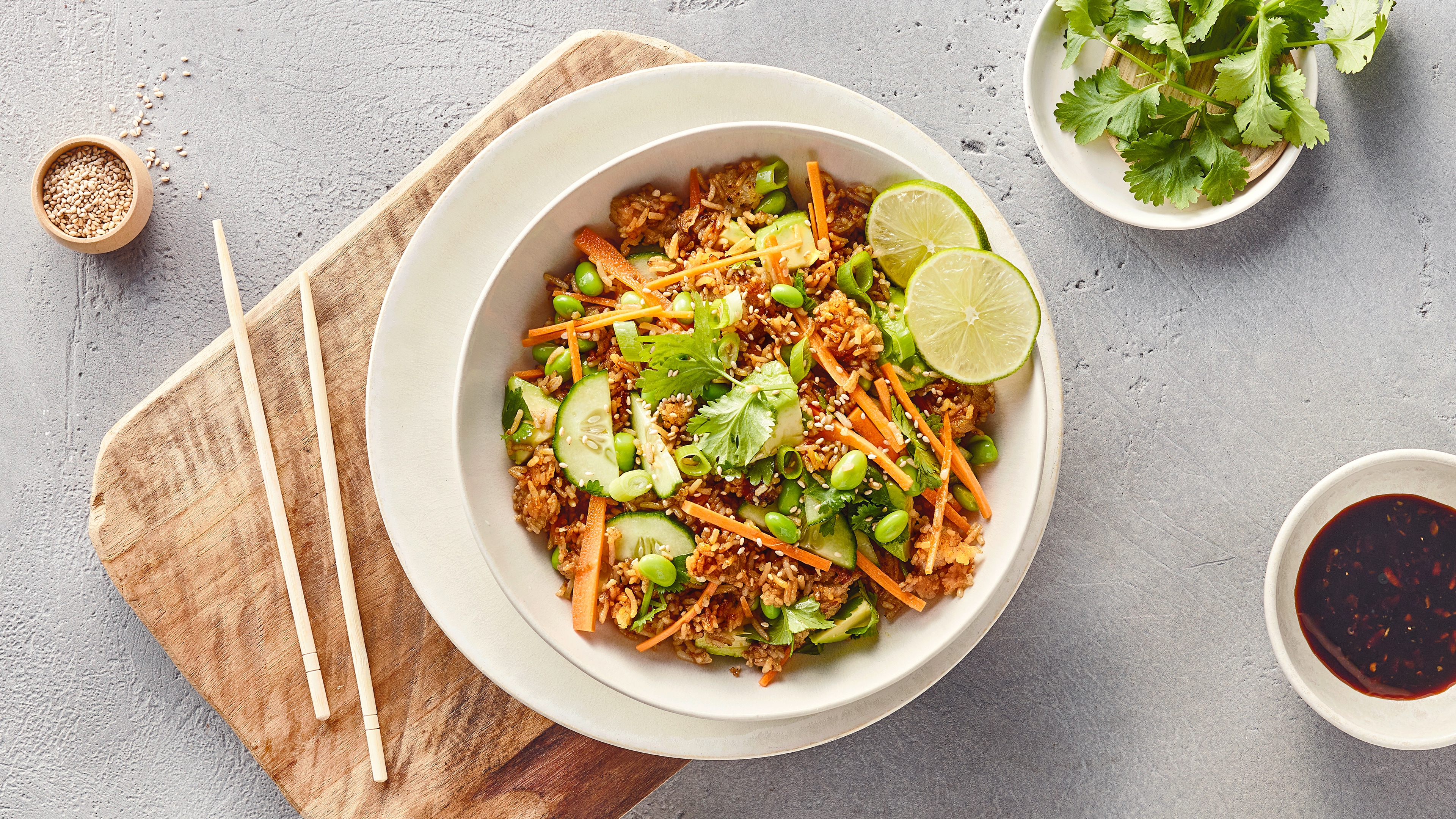 Rezept für Crispy Reis Salat Eine Schale mit Reis, Gurken- & Limettenscheiben, Karottenstreifen, Frühlingszwiebeln & Bohnen, garniert mit Sesam & Koriander