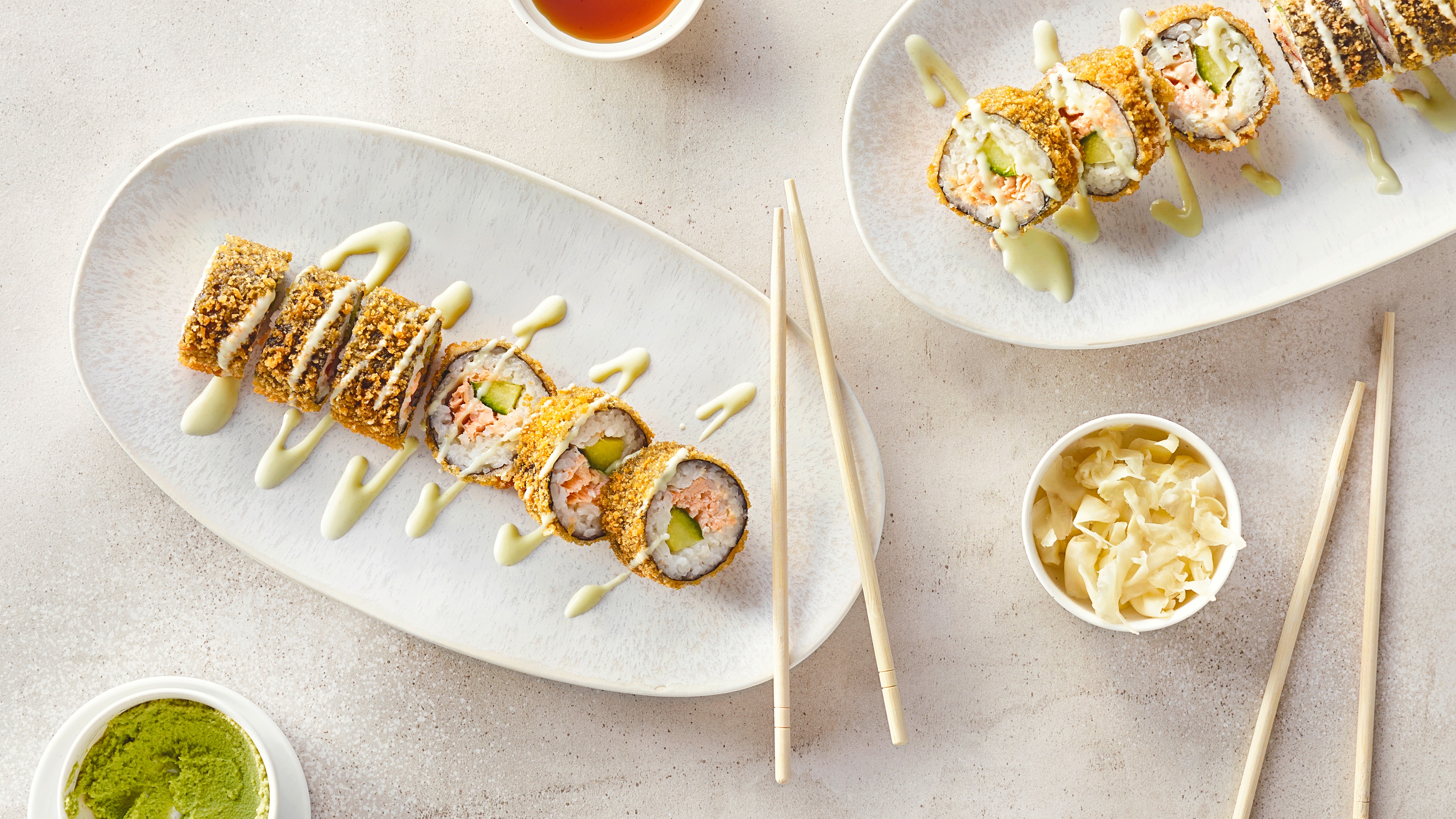 Rezept für Crispy Sushi mit Lachs Sushi, umwickelt mit Noriblättern, paniert, gefüllt mit Reis, Gurke und Lachs, getoppt mit heller Soße, auf einem Teller