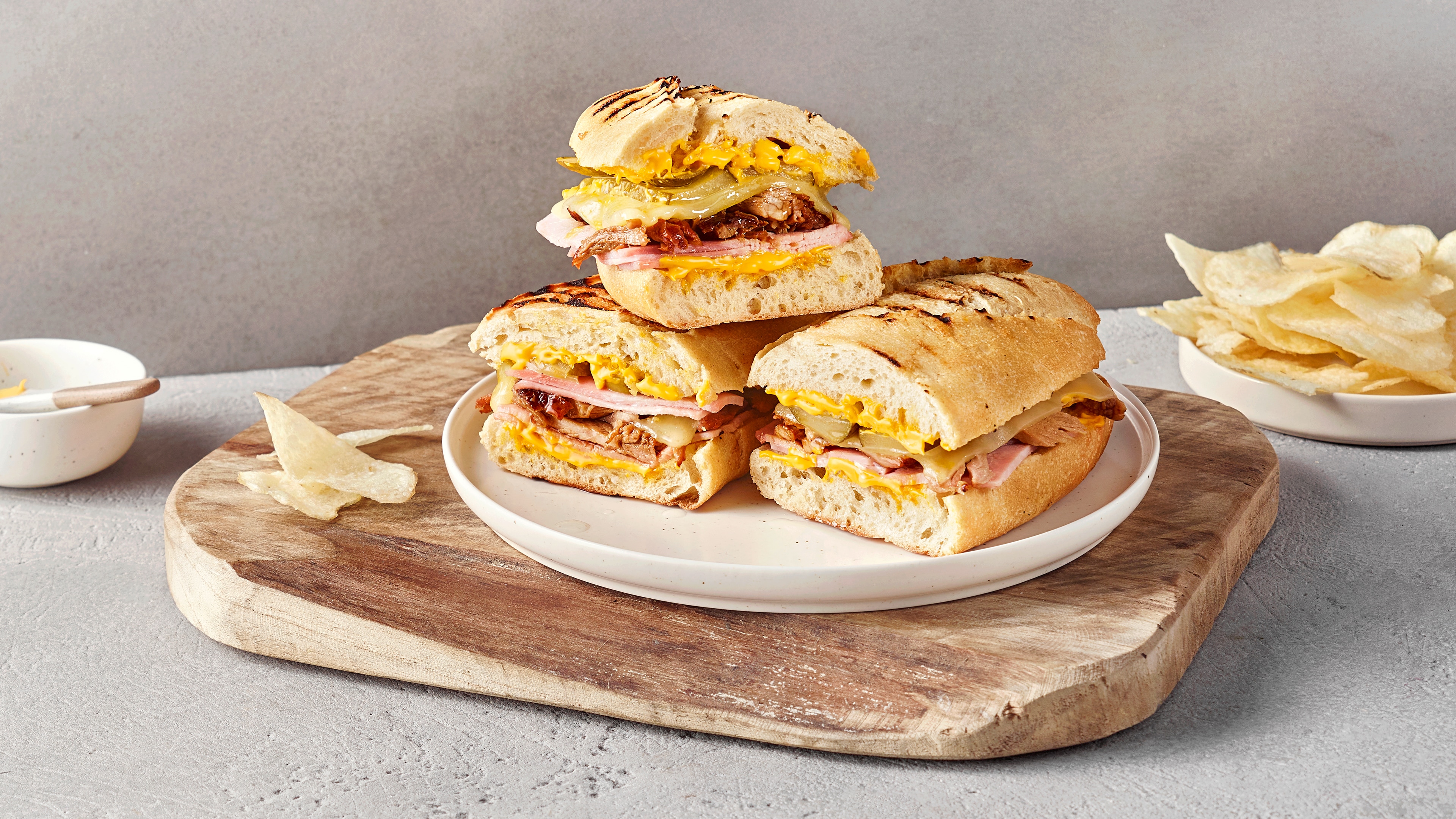 Ein Teller mit drei belegten Sandwichhälften, gefüllt mit Käse, Schinken, gebratenem Fleisch & eingelegten Gurkenscheiben.