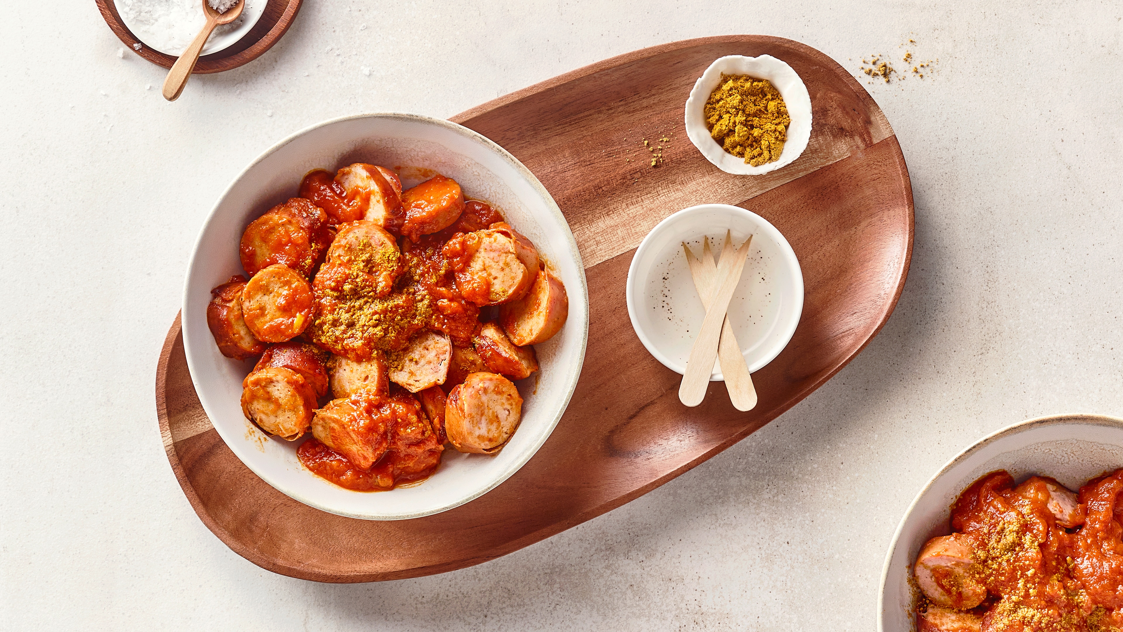 Eine Schale mit aufgeschnittenen Bratwürsten in roter Soße, bestreut mit gelbem Currypulver.