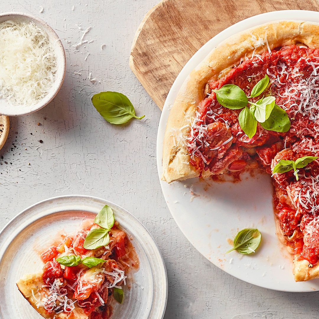 Ein Teller mit einer Pizza, bedeckt mit Tomatensauce, garniert mit grünen Basilikumblättern und feinem geriebenem Käse