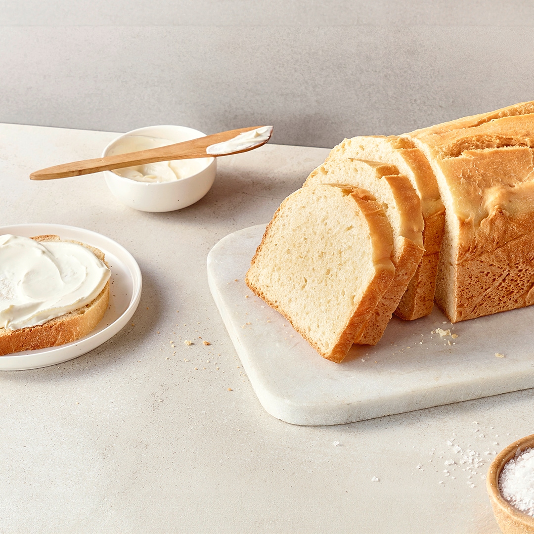 Fluffiges, helles Brot auf einer Steinplatte, daneben ein Teller mit einer Brotscheibe, bestrichen mit einer hellen Creme