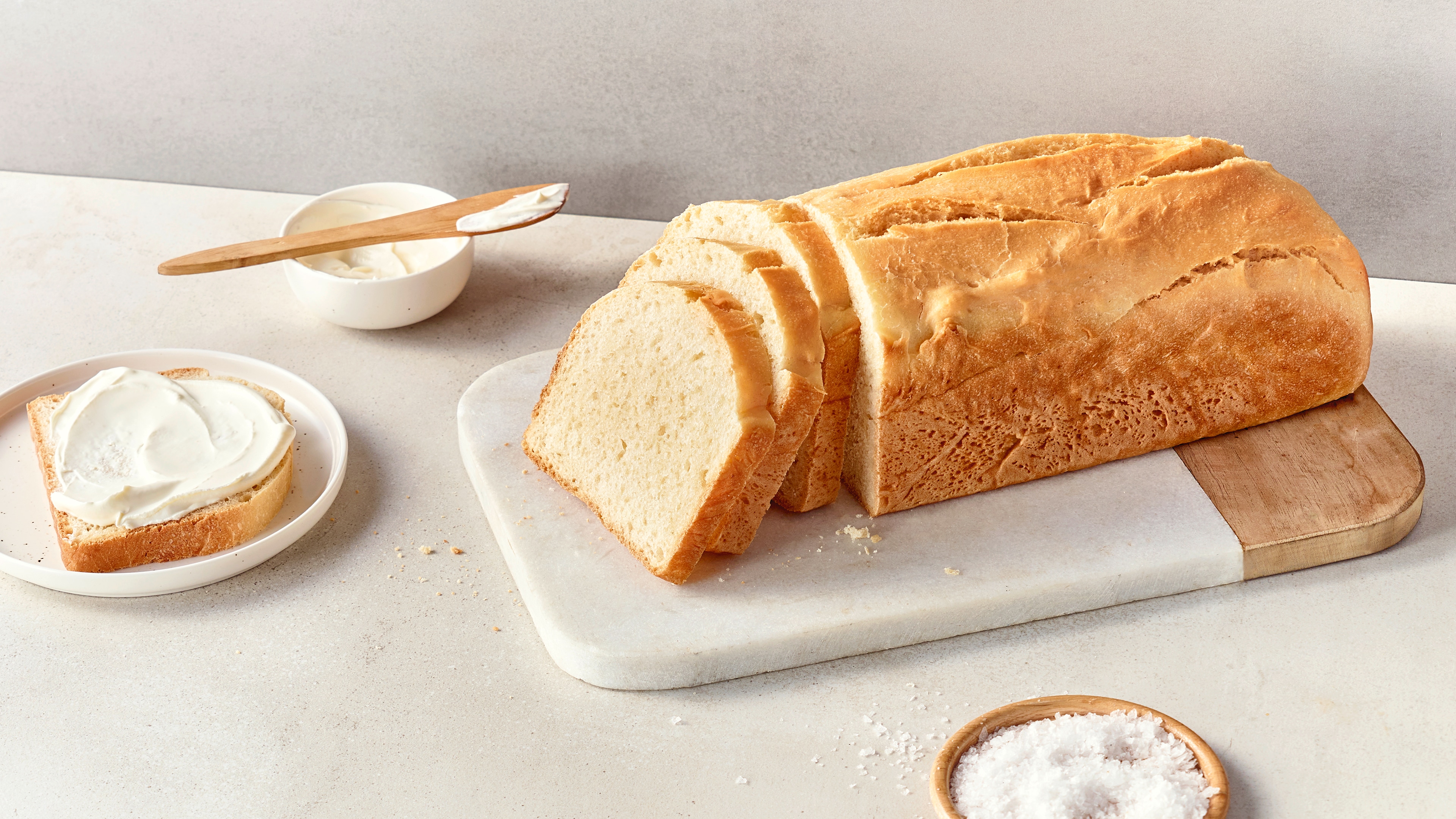 Fluffiges, helles Brot auf einer Steinplatte, daneben ein Teller mit einer Brotscheibe, bestrichen mit einer hellen Creme