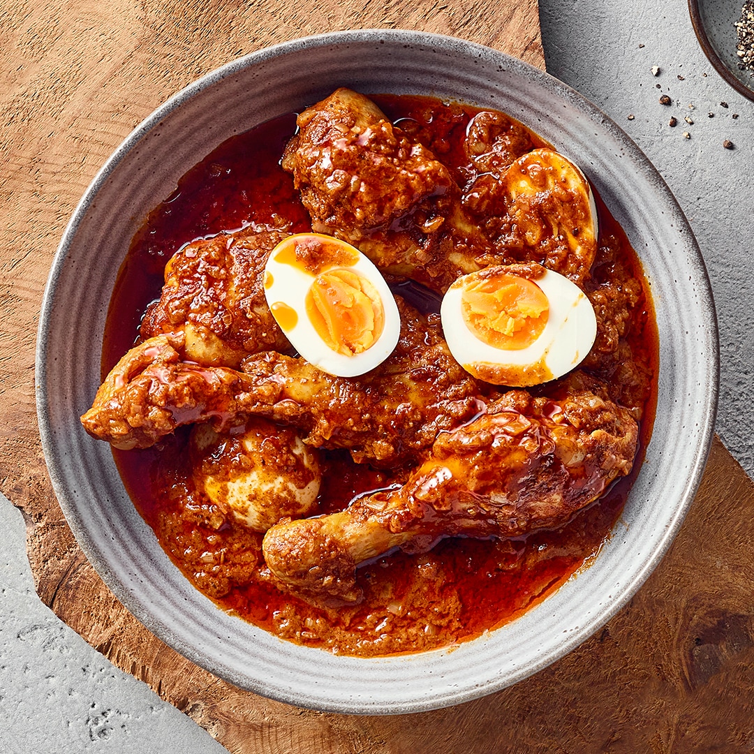 Ein Teller mit Hähnchenschenkeln in dicker roter Soße, darauf zwei halbierte gekochte Eier.