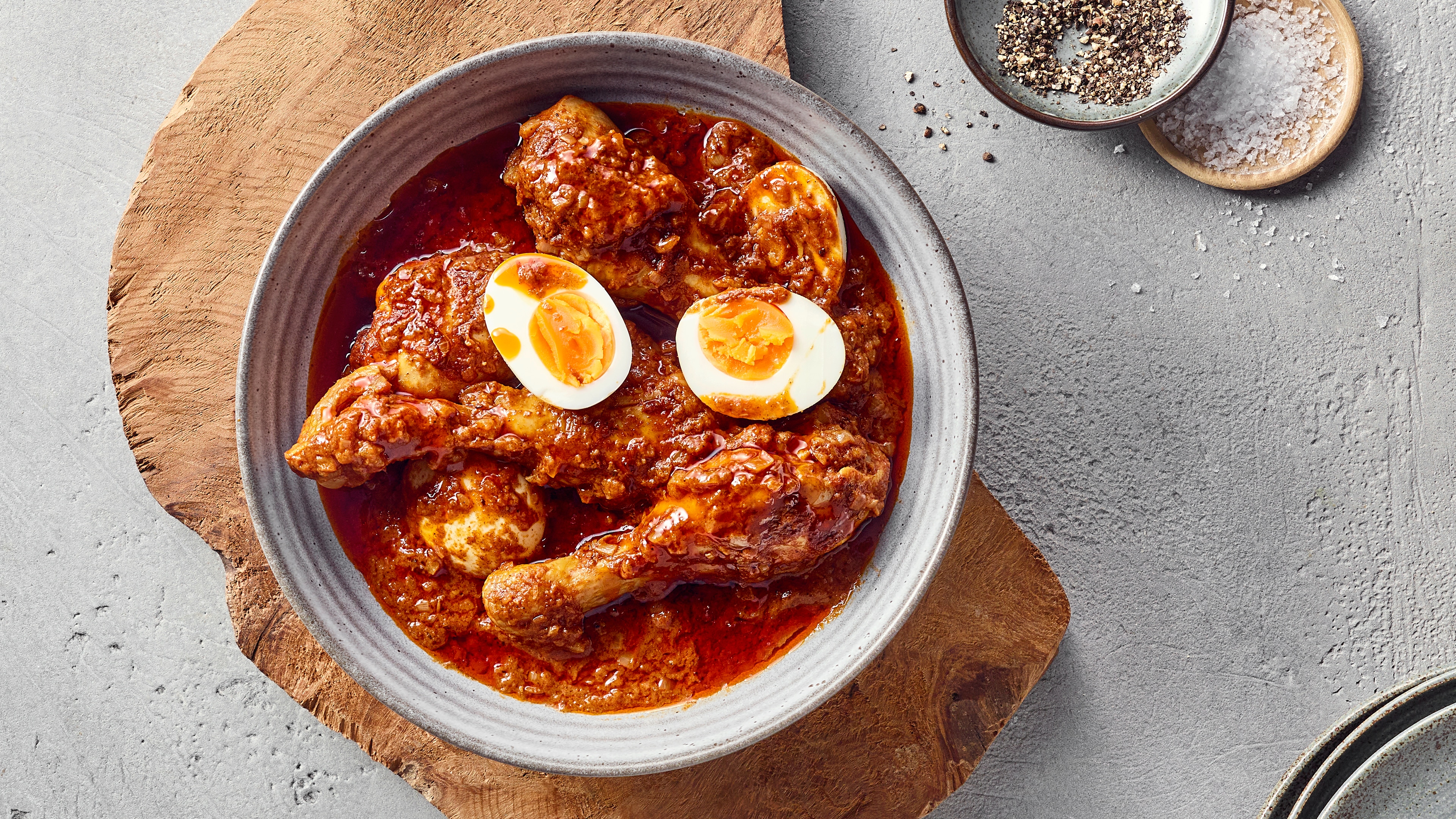 Ein Teller mit Hähnchenschenkeln in dicker roter Soße, darauf zwei halbierte gekochte Eier.