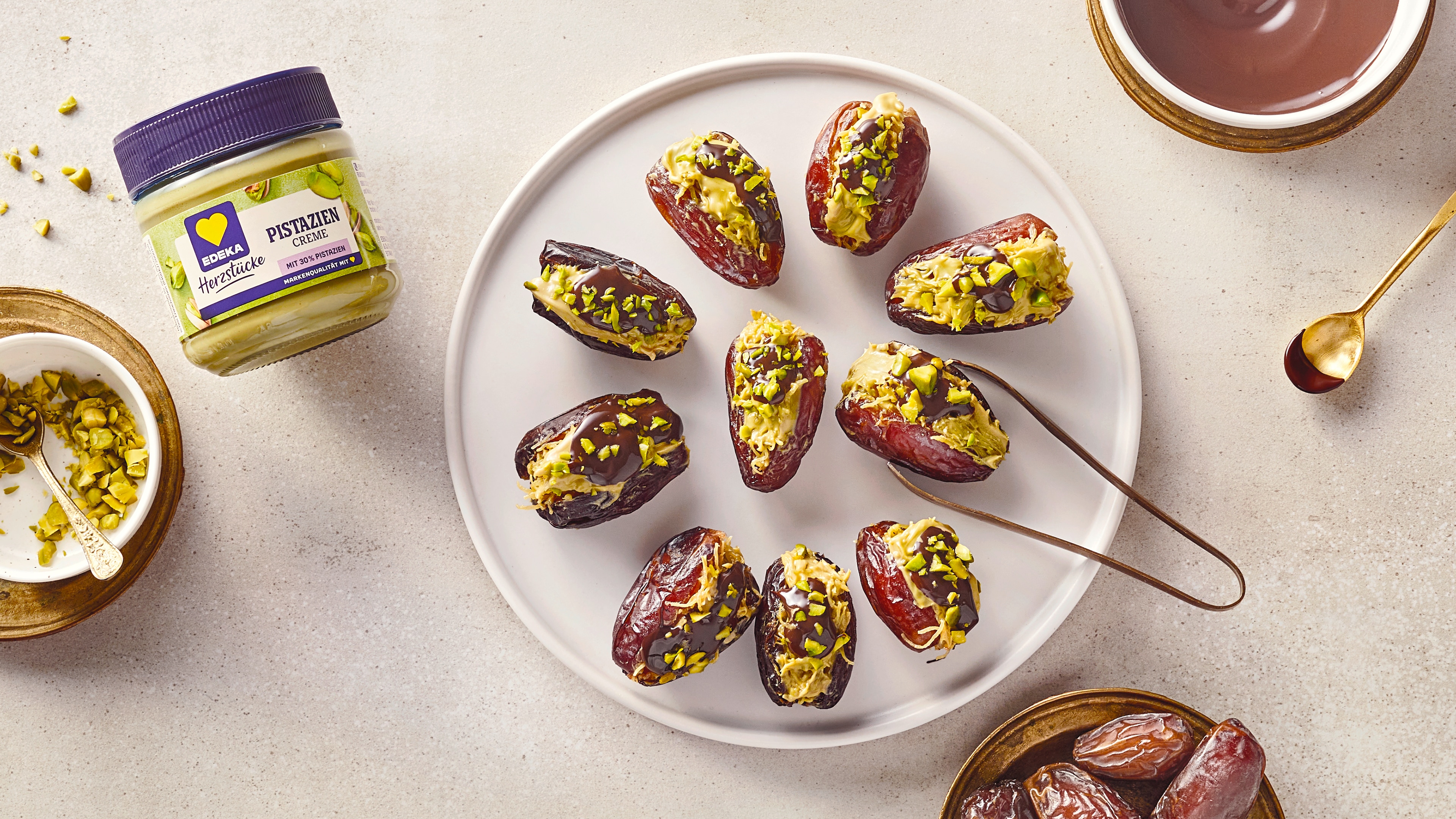 Rezept für Dubai Datteln mit EDEKA Herzstücke Pistazien Creme Ein Teller mit aufgeschnittenen Datteln, gefüllt mit heller, grüner Creme, daneben EDEKA Herzstücke Pistazien Creme