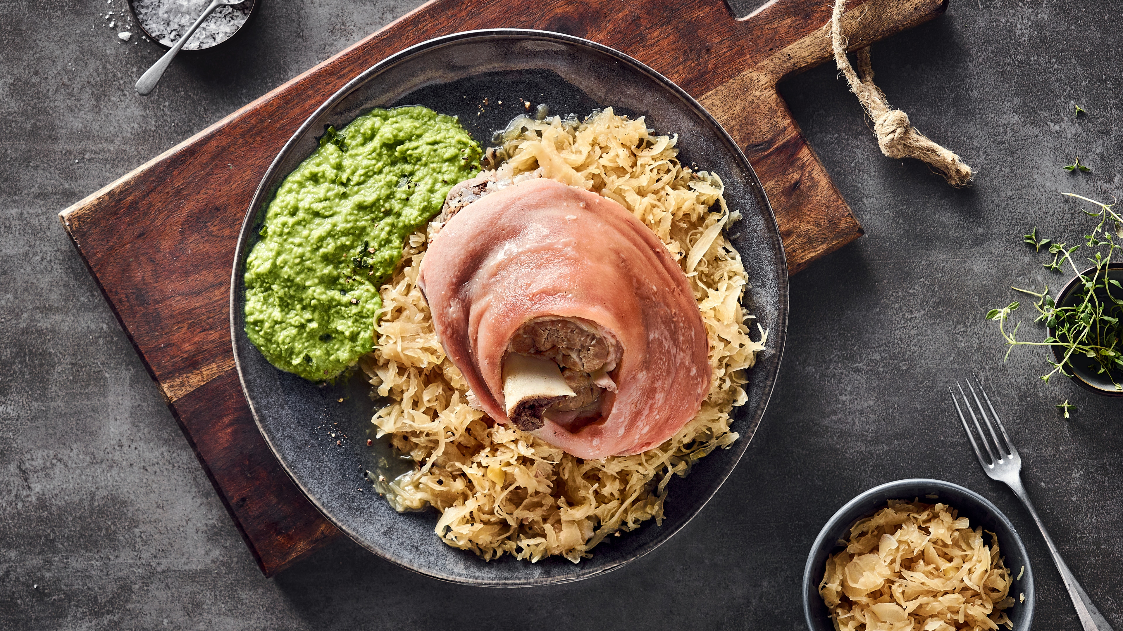 Rezept für Eisbein mit Sauerkraut und Erbsenpüree Ein Teller mit einem hellen, runden Stück Fleisch, gebettet auf Sauerkraut, dazu cremiges, kräftig grünes Püree