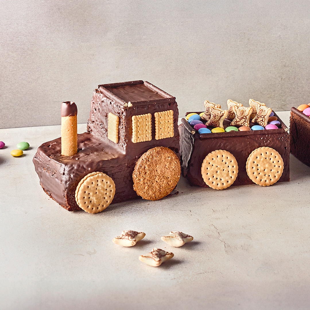 Ein Kuchen in Form einer Eisenbahn, überzogen mit Kuvertüre, mit Reifen und Fenstern aus Keksen, Wagen gefüllt mit Smarties