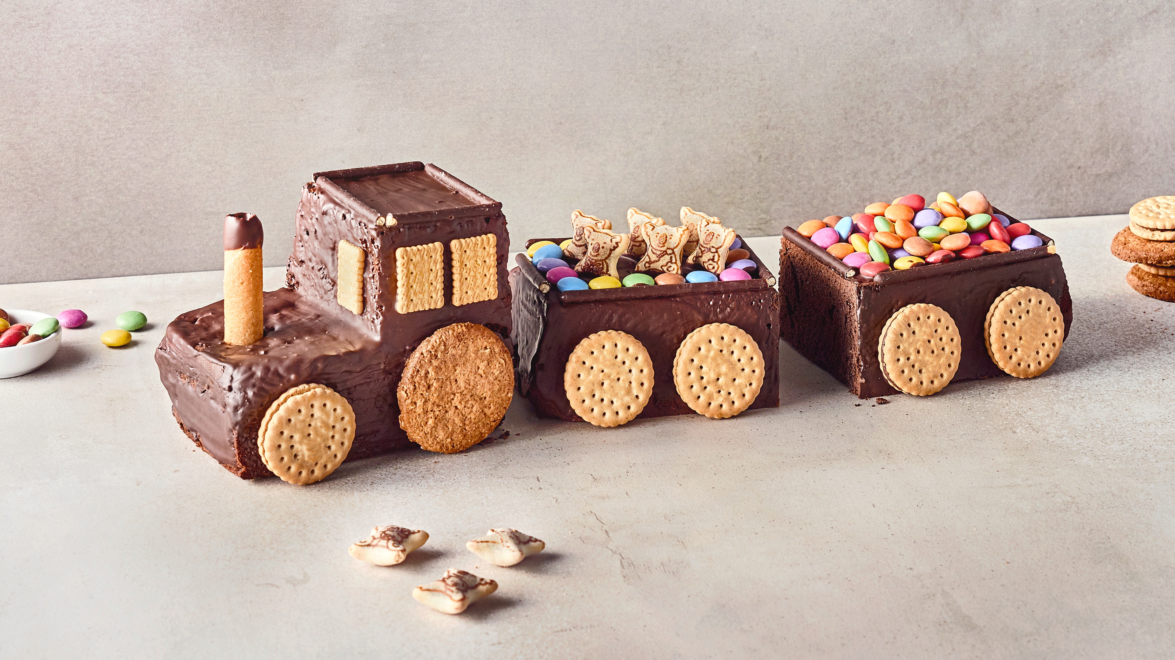 Rezept für einen Eisenbahn-Kuchen Ein Kuchen in Form einer Eisenbahn, überzogen mit Kuvertüre, mit Reifen und Fenstern aus Keksen, Wagen gefüllt mit Smarties