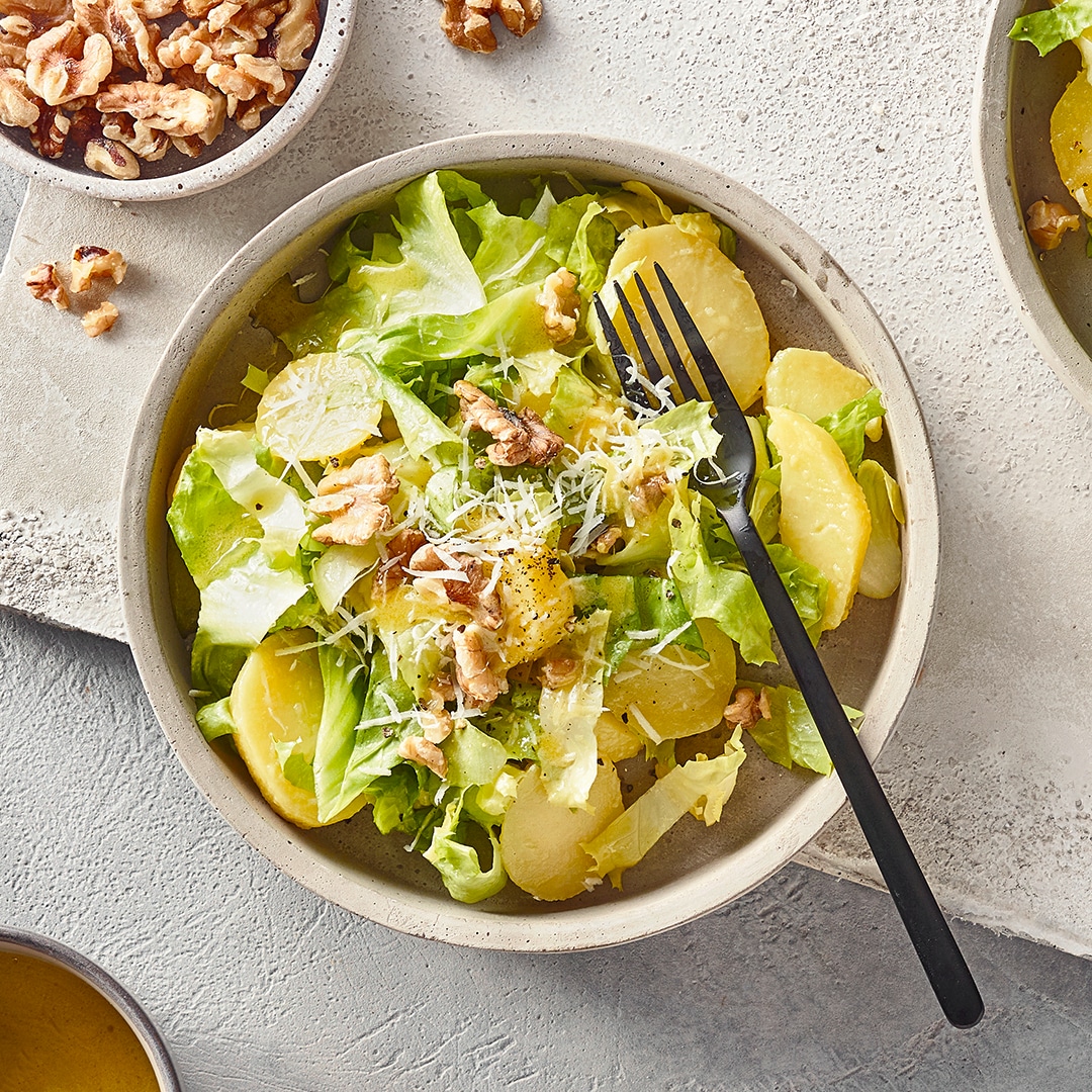 Eine Schüssel mit grünem Blattsalat, Kartoffelscheiben, geriebenem Käse und Walnussstücken