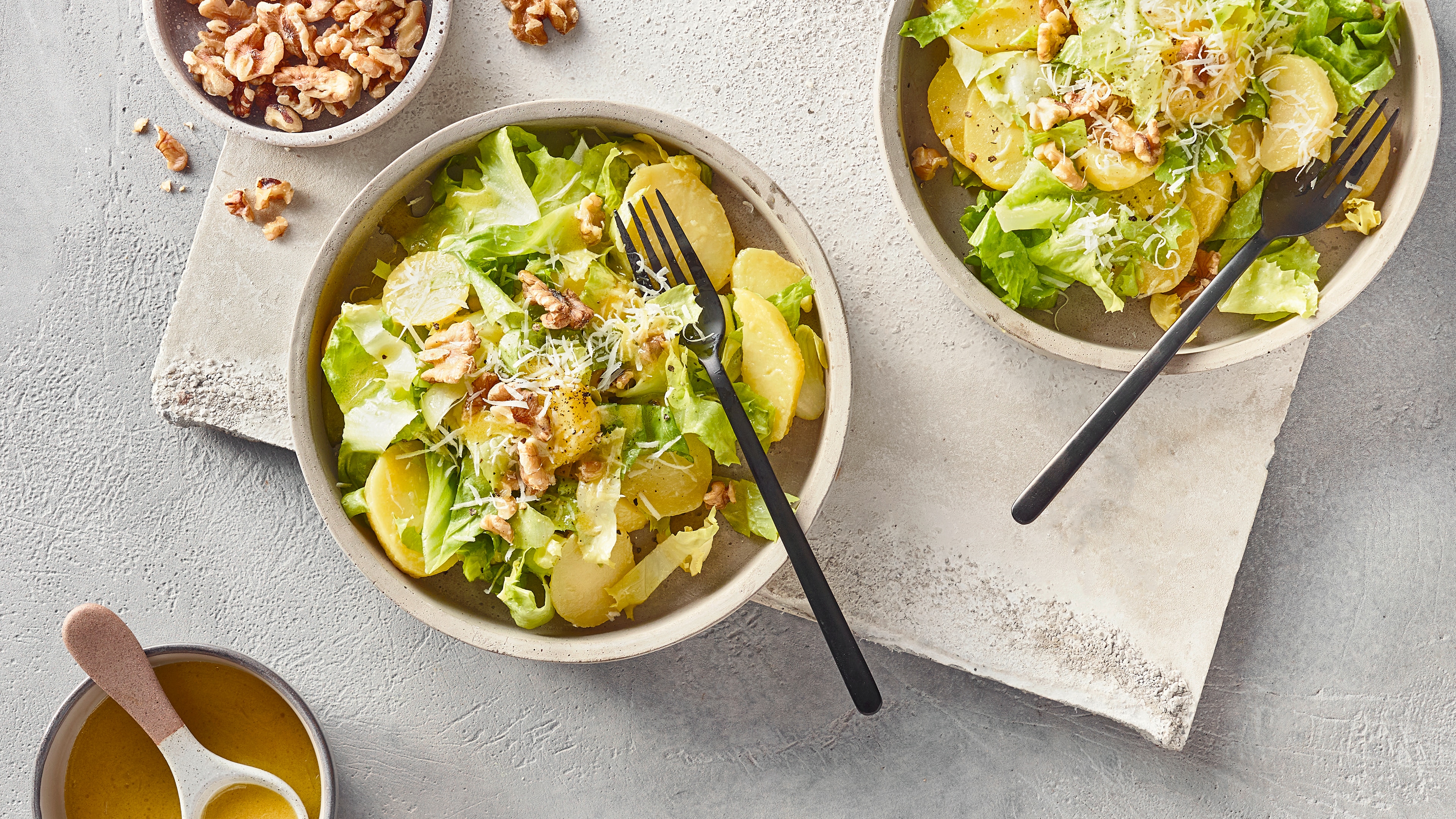 Rezept für Endiviensalat mit Kartoffeln Eine Schüssel mit grünem Blattsalat, Kartoffelscheiben, geriebenem Käse und Walnussstücken