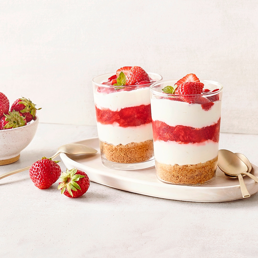 Dessertgläser mit Schichten aus Creme, Erdbeeren und Keksboden, garniert mit frischen Erdbeeren und Minze.