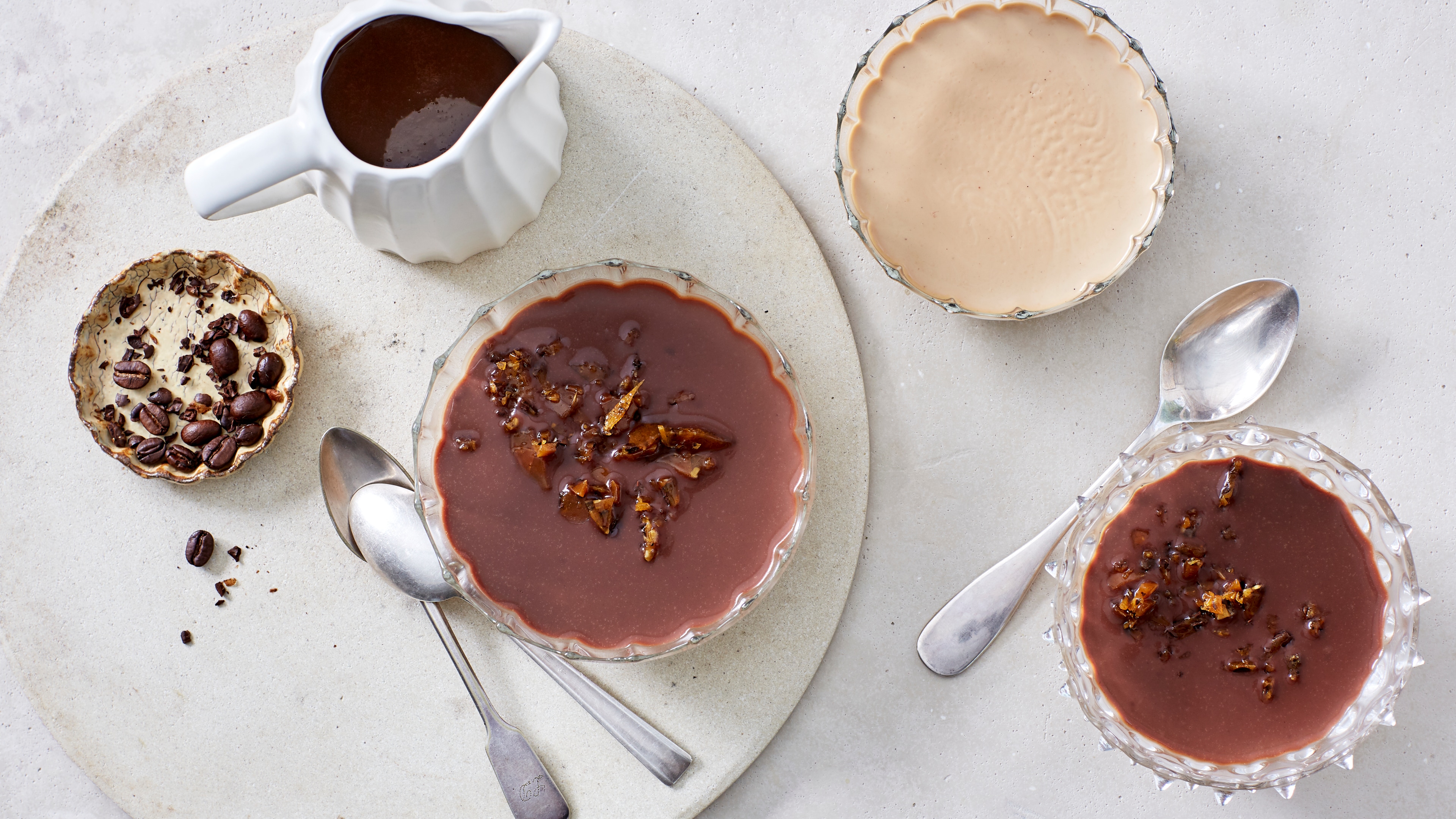 Glasschälchen, gefüllt mit heller, fester Creme,  getoppt mit einer dunklen Schokoschicht und Karamellstückchen