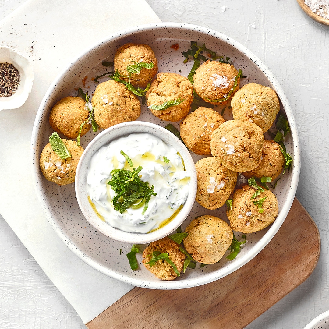 Schale mit vielen frittierten Bällchen und einer weißen Creme zum Dippen. Mit Grünzeug verfeinert.