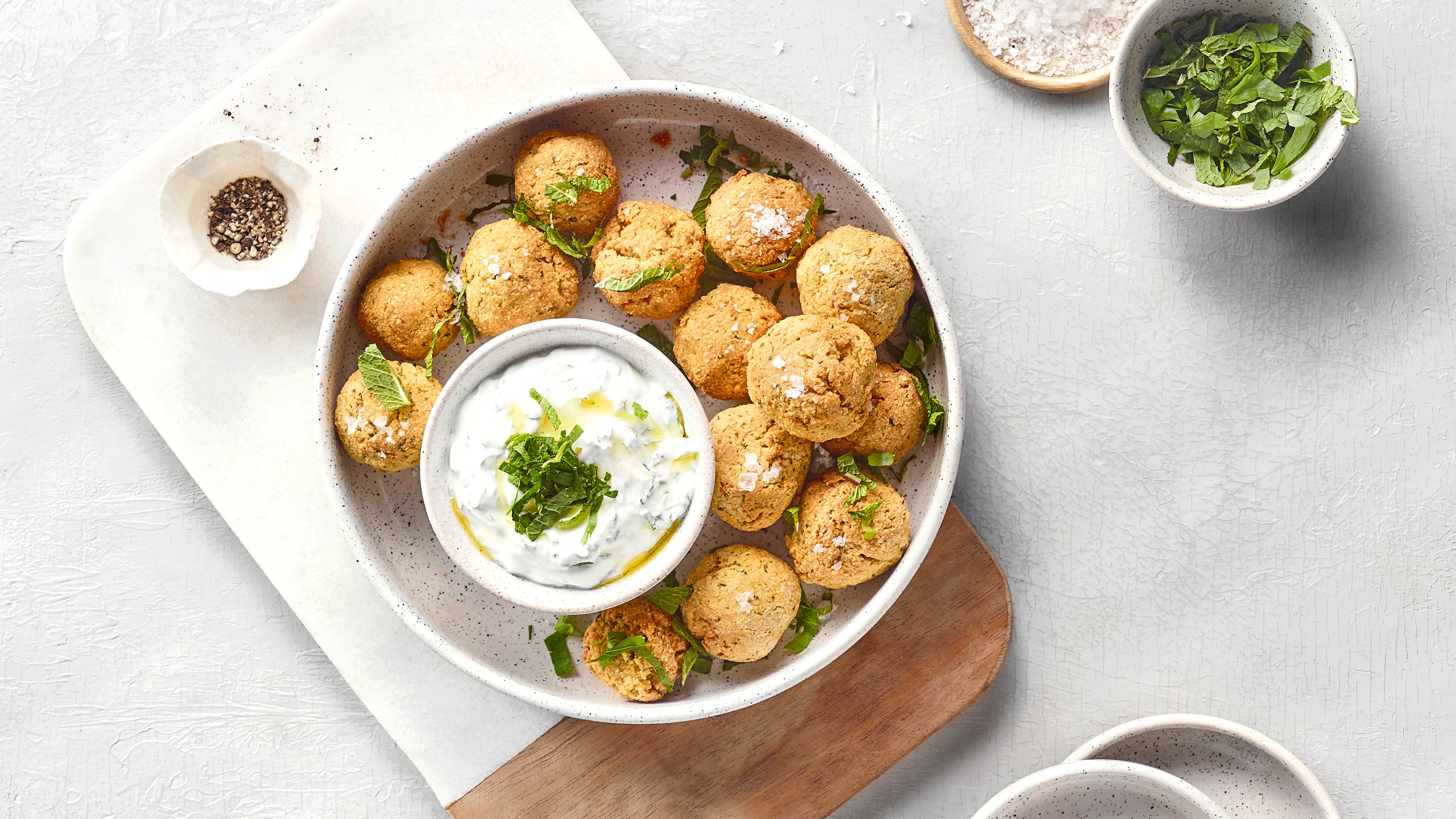 Schale mit vielen frittierten Bällchen und einer weißen Creme zum Dippen. Mit Grünzeug verfeinert.