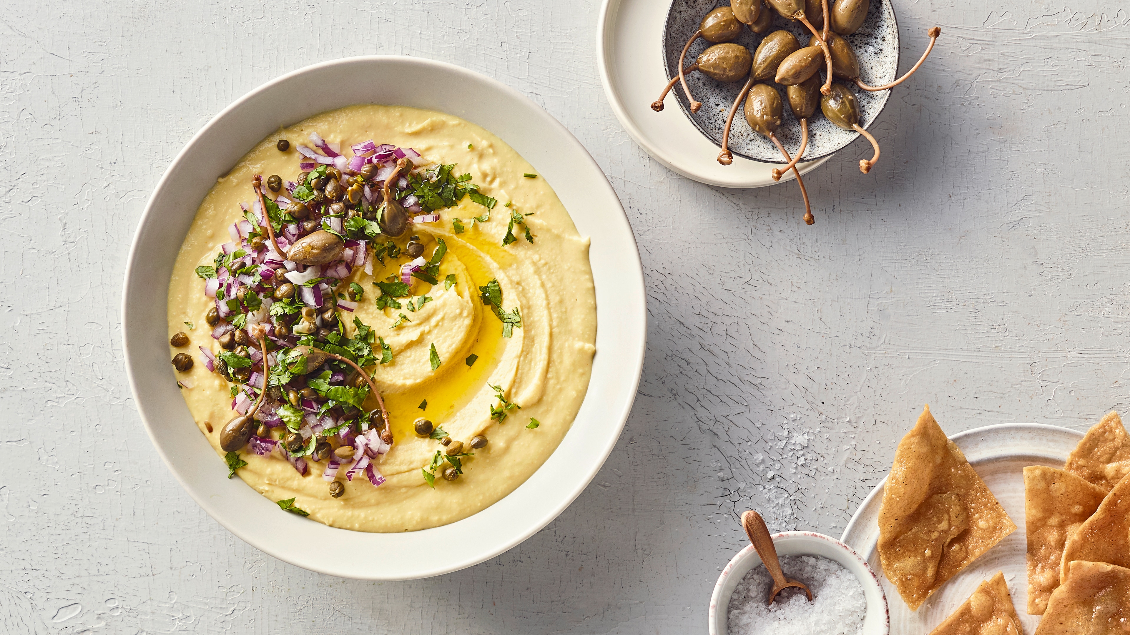 Eine Schale mit cremigem Aufstrich, garniert mit gehackten roten Zwiebeln, grünen Kräutern, Kapern und etwas Öl
