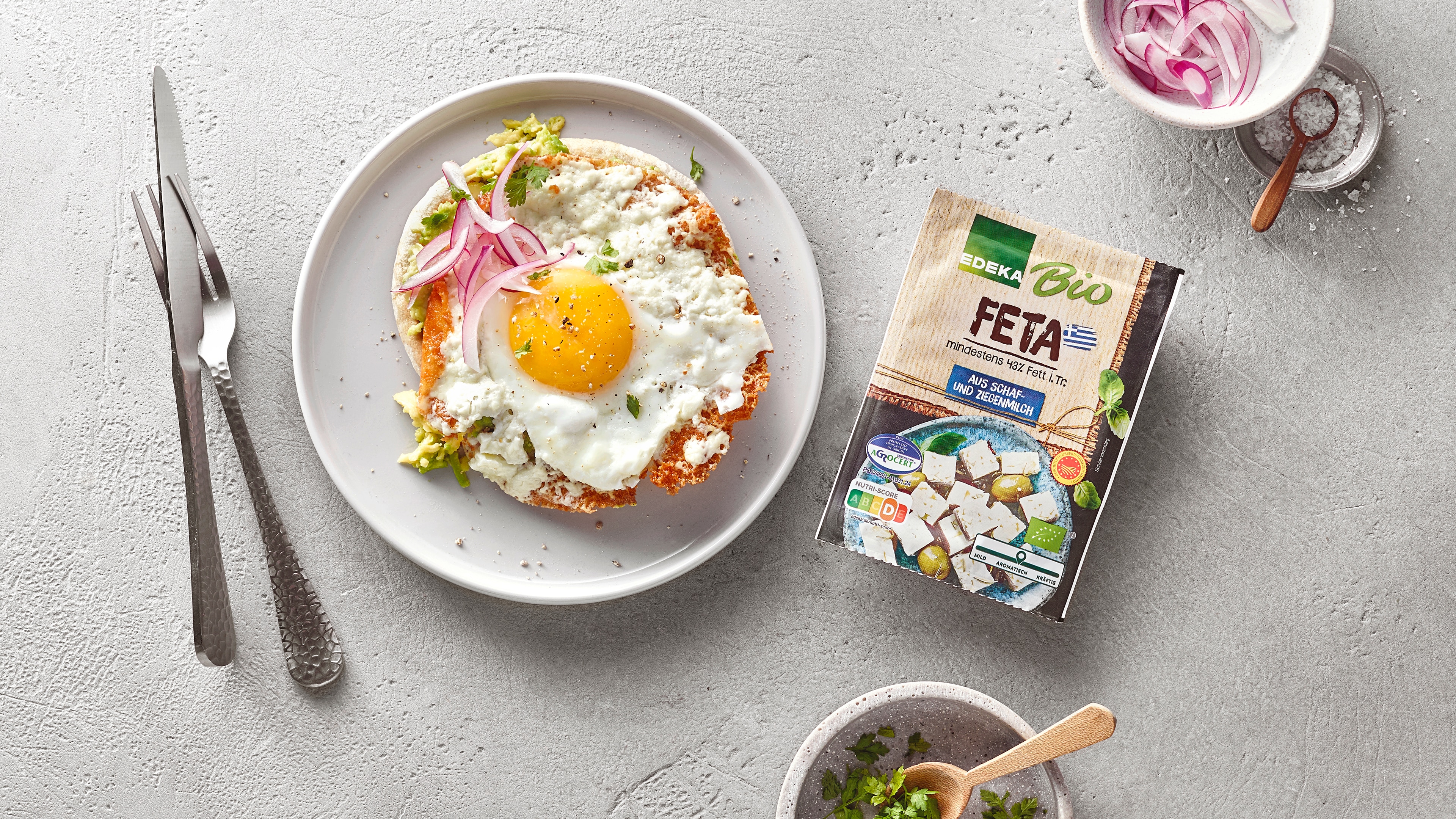 Flaches Brot mit Spiegelei, Feta und Zwiebeln. Rechts daneben EDEKA Bio Feta.