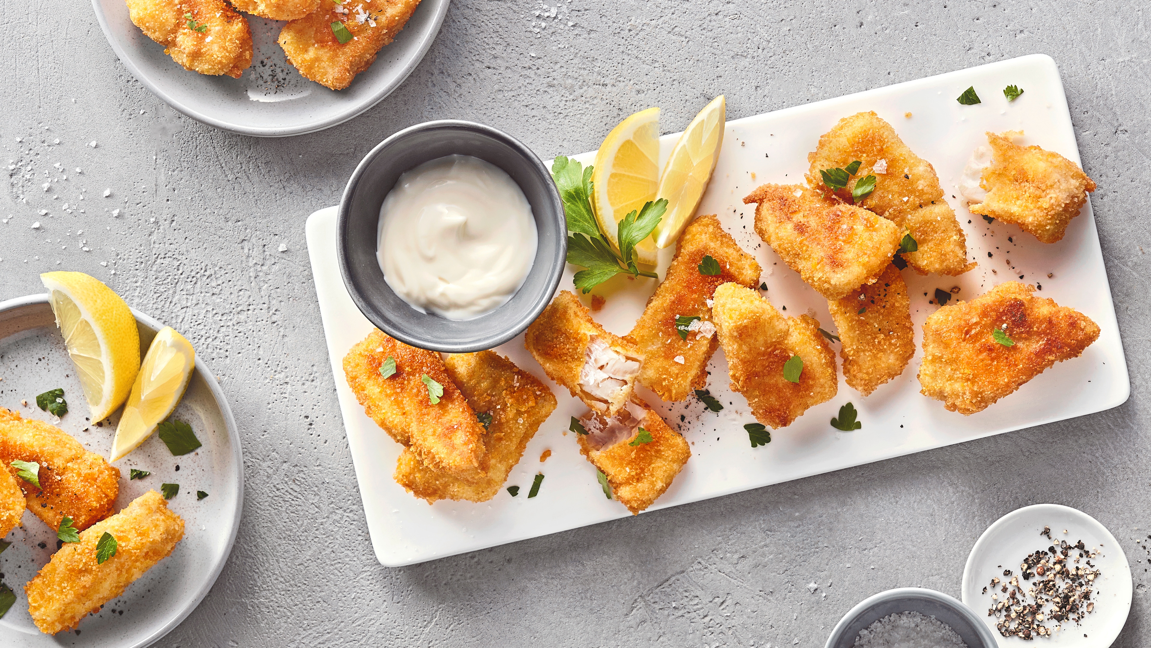 Ein Teller mit goldbraun frittierten Fischnuggets, daneben eine Schale mit hellem Dip.