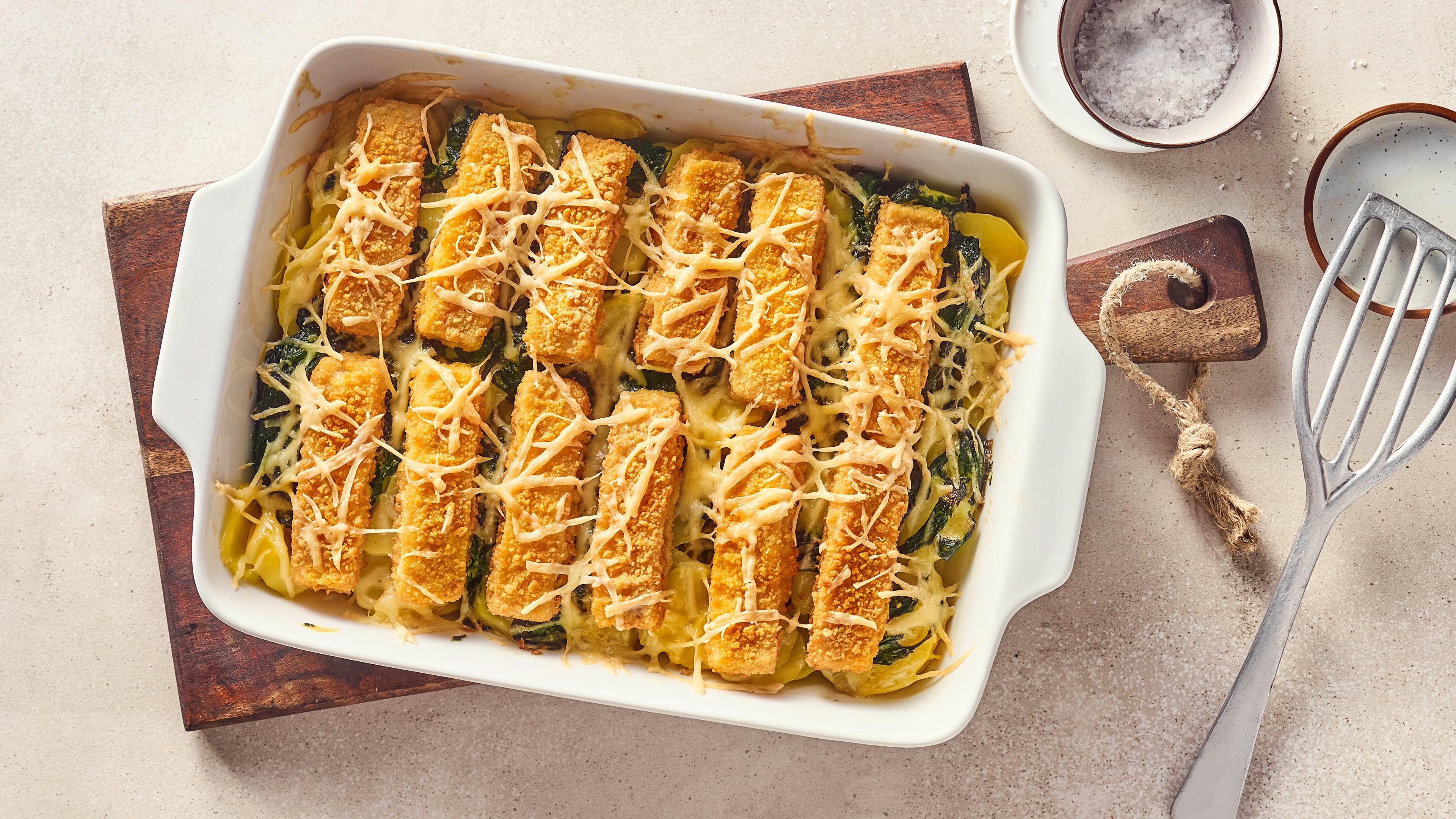 Rezept für Fischstäbchen-Auflauf Eine Keramikauflaufform mit Kartoffelscheiben, Spinat und knusprigen Fischstäbchen, überbacken mit Käse