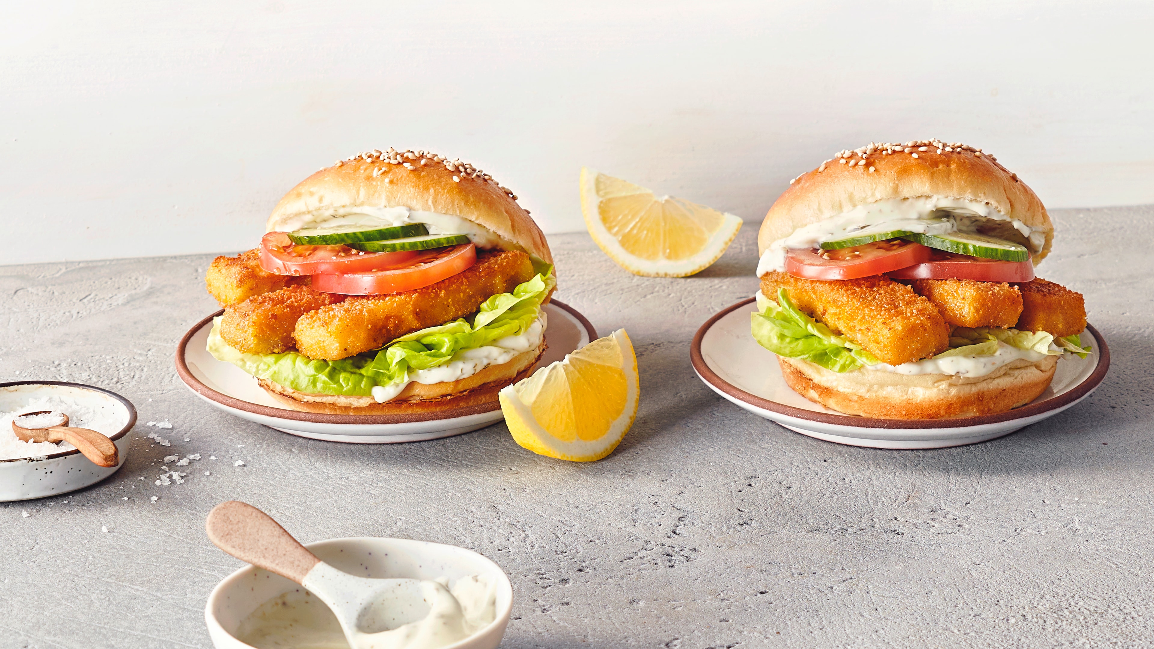 Zwei aufgeklappte Burger mit Salat, Tomaten, Gurken und Fischstäbchen
