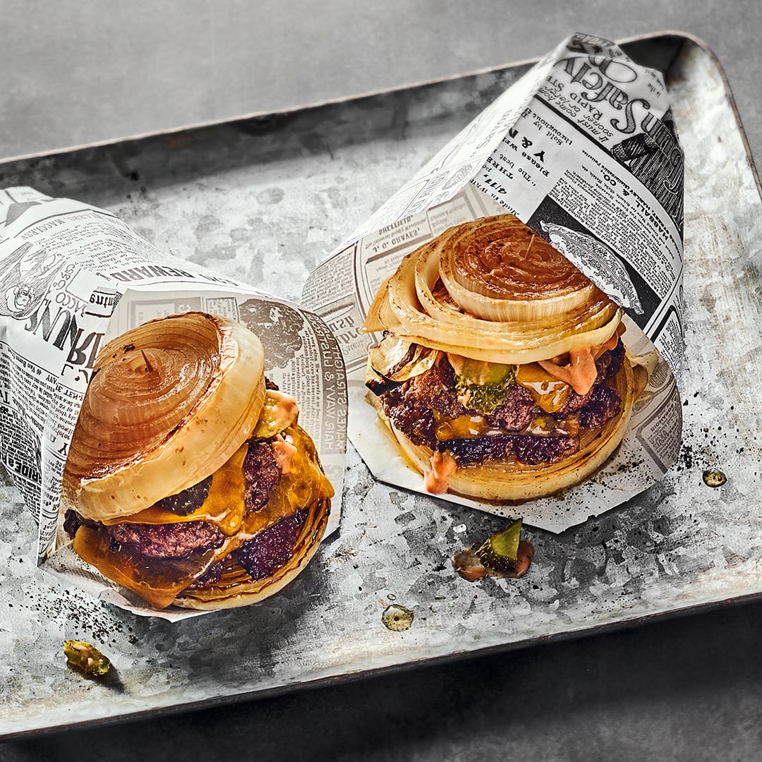 Brotloser Cheeseburger mit karamellisierten Zwiebelscheiben und saftigem Rind-Patty, gewickelt in Zeitungspapier.