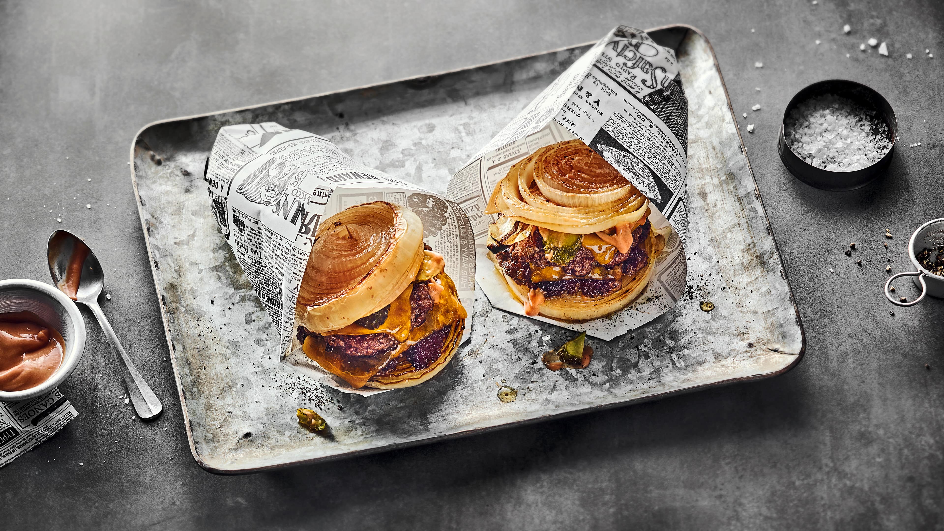 Rezept für Flying Dutchman Burger Brotloser Cheeseburger mit karamellisierten Zwiebelscheiben und saftigem Rind-Patty, gewickelt in Zeitungspapier.