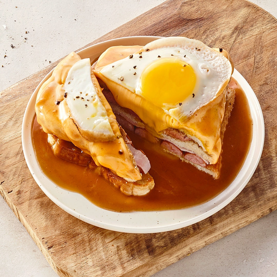 Teller mit bräunlicher Soße und einem gestapelten Toast mit Schinken, Käse und Spiegelei