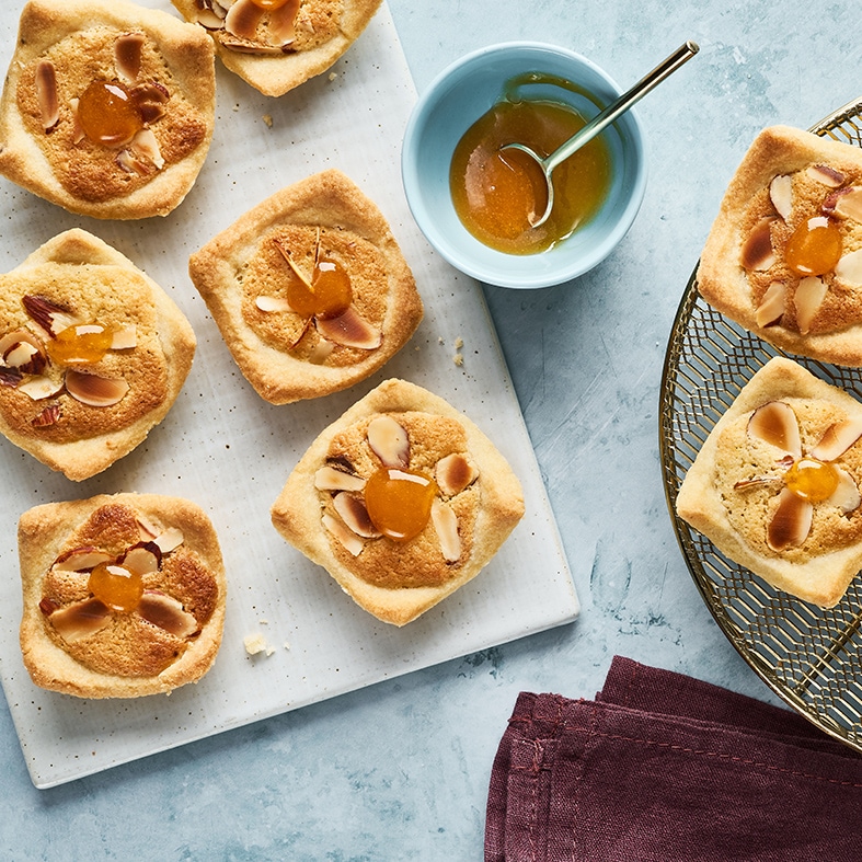 Kleine Gebäckstücke mit Mandelblättchen und einem Schälchen mit oranger Marmelade