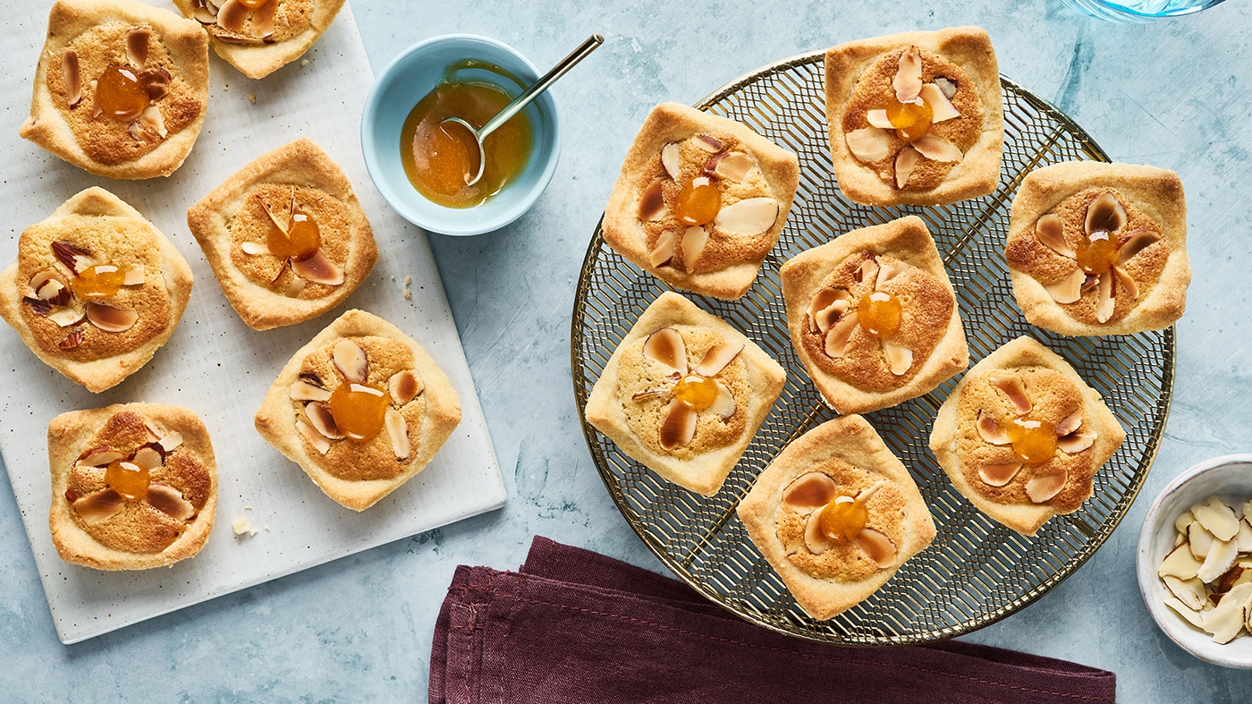 Kleine Gebäckstücke mit Mandelblättchen und einem Schälchen mit oranger Marmelade