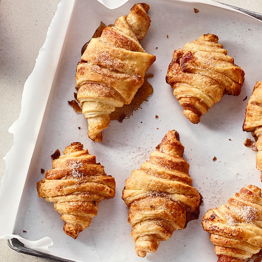 Ein Blech mit mehreren Croissants aus Blätterteig, goldbraun gebacken und mit feinem Zucker bestreut.