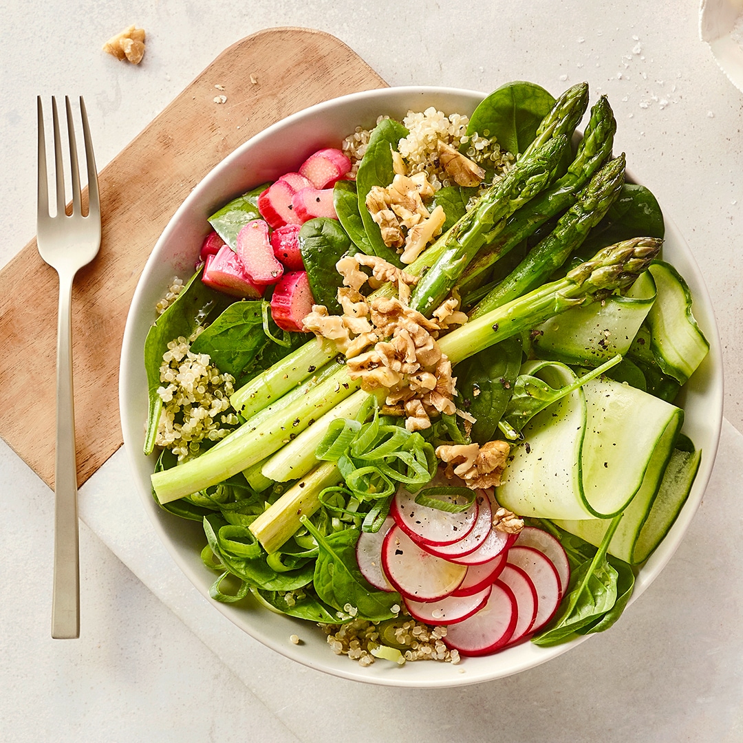 Eine Schale mit grünem Spargel, Gurkenscheiben, Radieschen, Spinat, Frühlingszwiebeln, Walnüssen und etwas Quinoa.