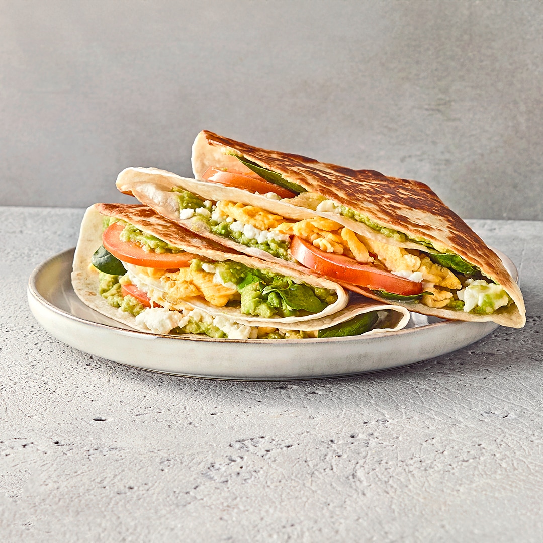 Ein Teller mit braun angebratenen, gefalteten Wraps, gefüllt mit grüner Soße, Mozzarella, Salat, Tomate und Rührei