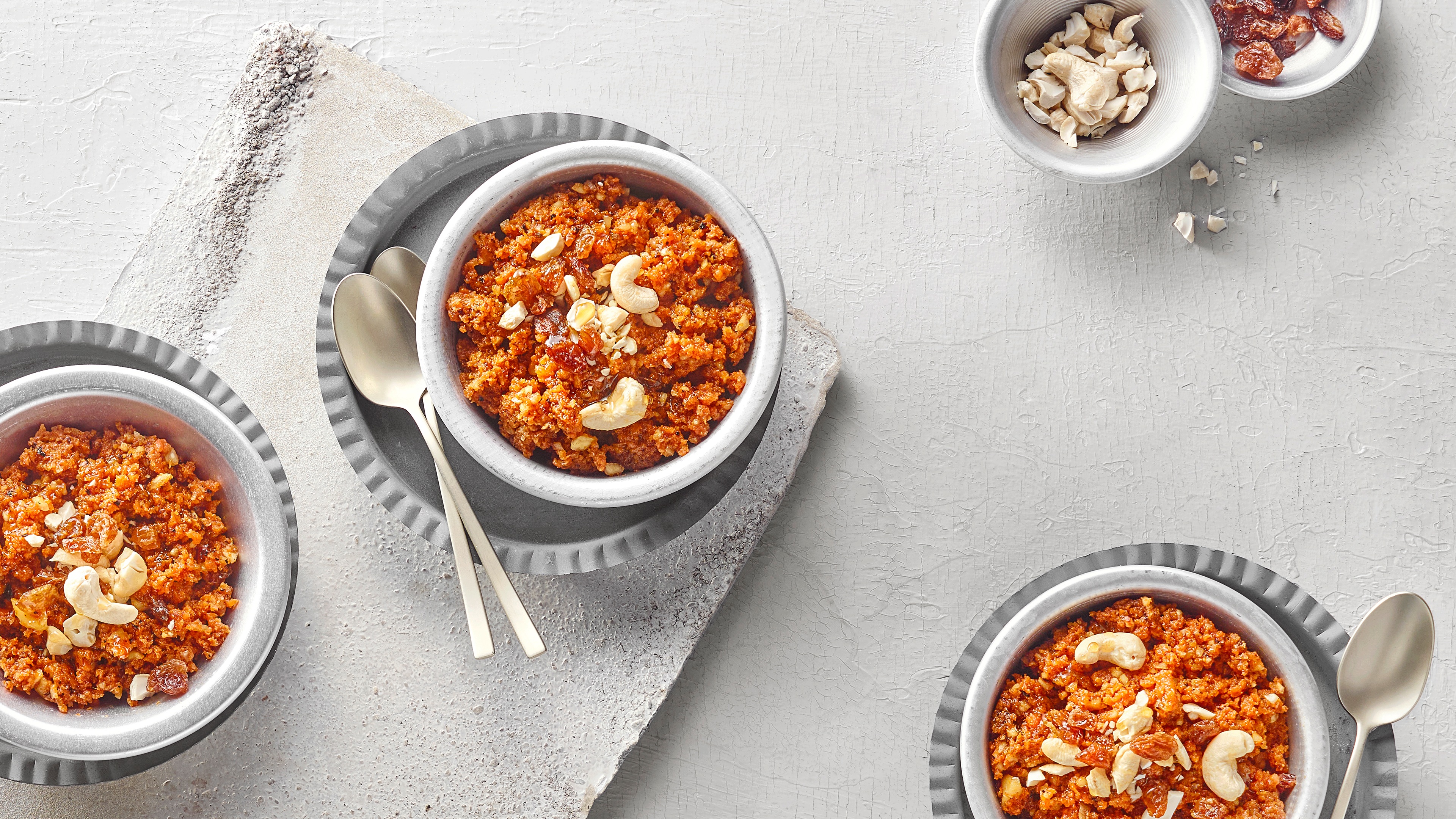 Drei Puddingschalen mit geraspelten Möhren, Trockenfrüchten und Cashewnüssen.