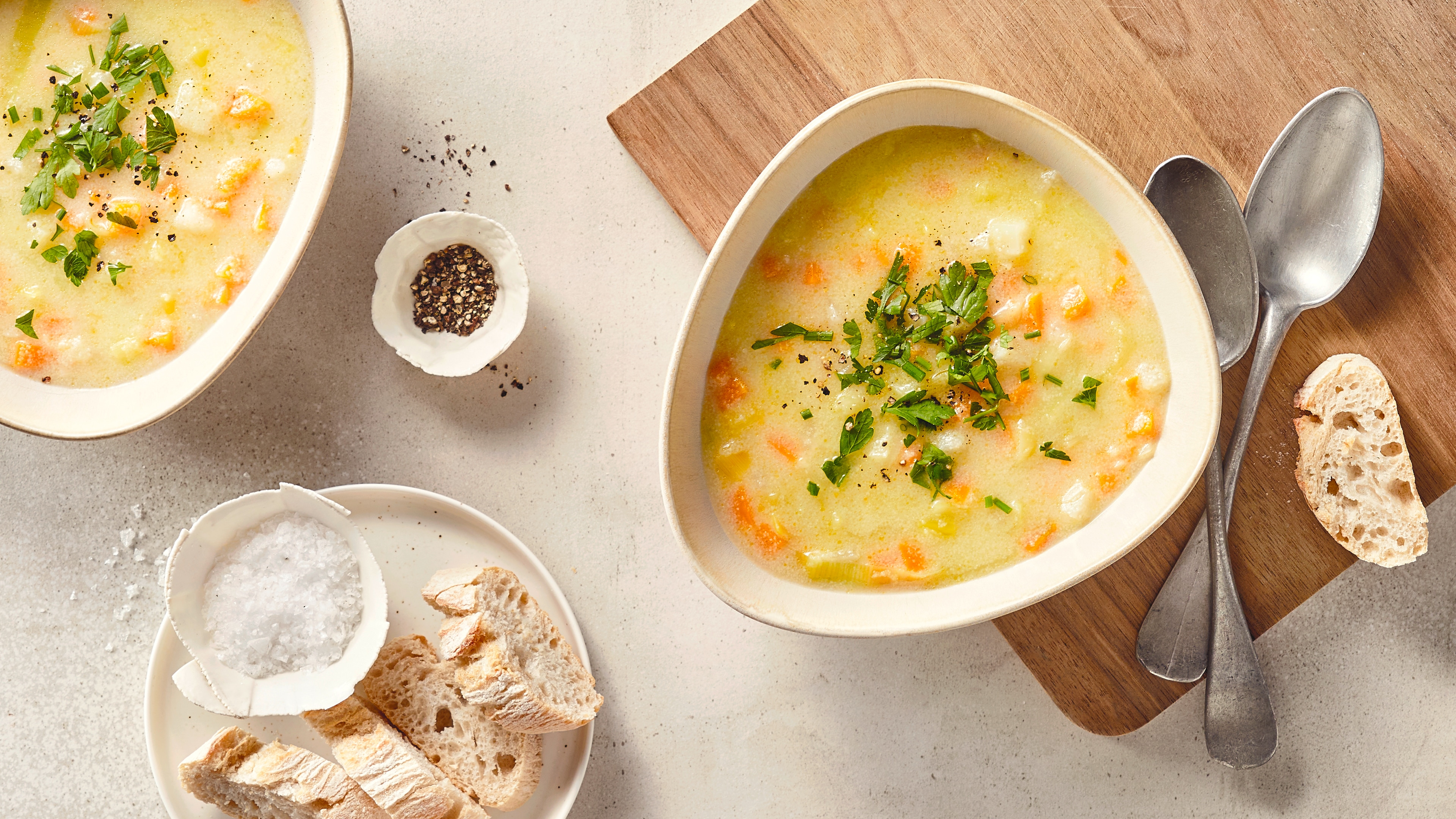 Rezept für gebrannte Griesssuppe Eine Schale mit einer hellen Suppe, mit Karottenstücken und Lauch, garniert mit gehackter Petersilie, daneben ein Stück Brot